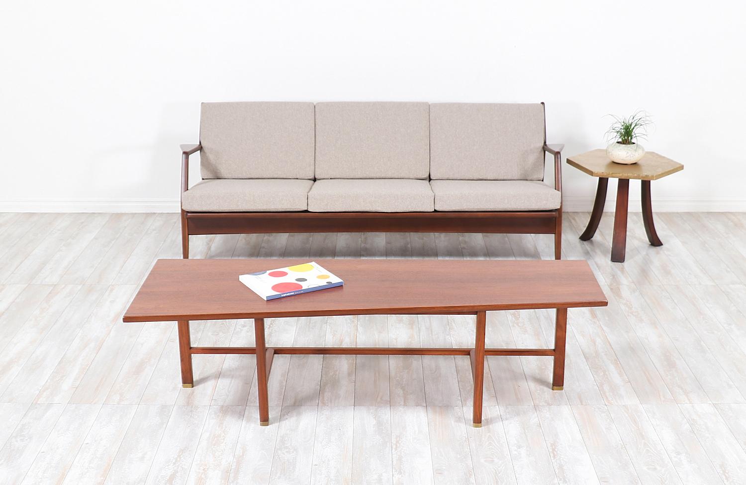 Beautiful coffee table designed by Edward J. Wormley for Dunbar in the United States circa 1950s. This fascinating coffee table features a sturdy walnut wood frame with intersecting stretchers at the base and rectangular brass caps on the feet tips.