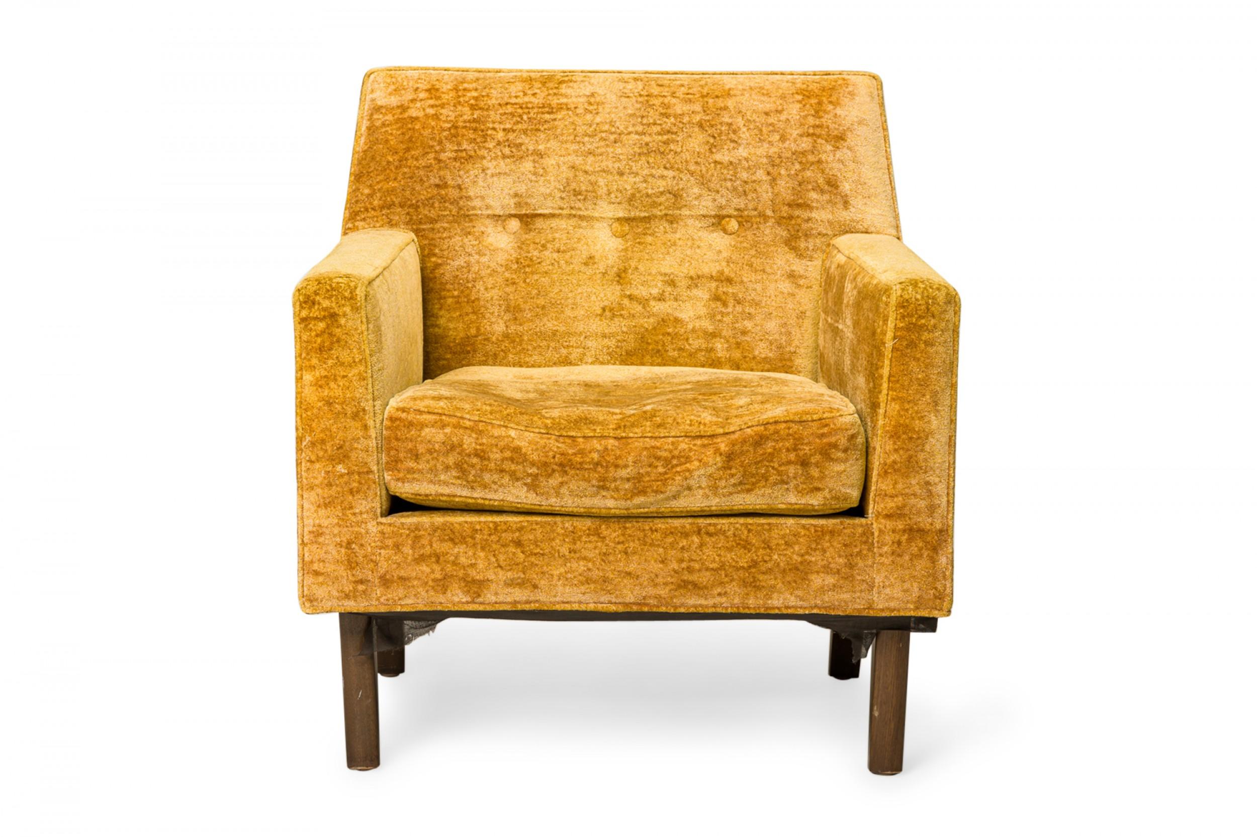 Amerikanischer Loungesessel aus der Mitte des Jahrhunderts mit quadratischen Armlehnen und einer sich leicht verjüngenden, kurzen Rückenlehne. Der Sessel ist mit goldfarbenem Velours gepolstert und hat ein mit Knöpfen besetztes Rückenkissen, das auf