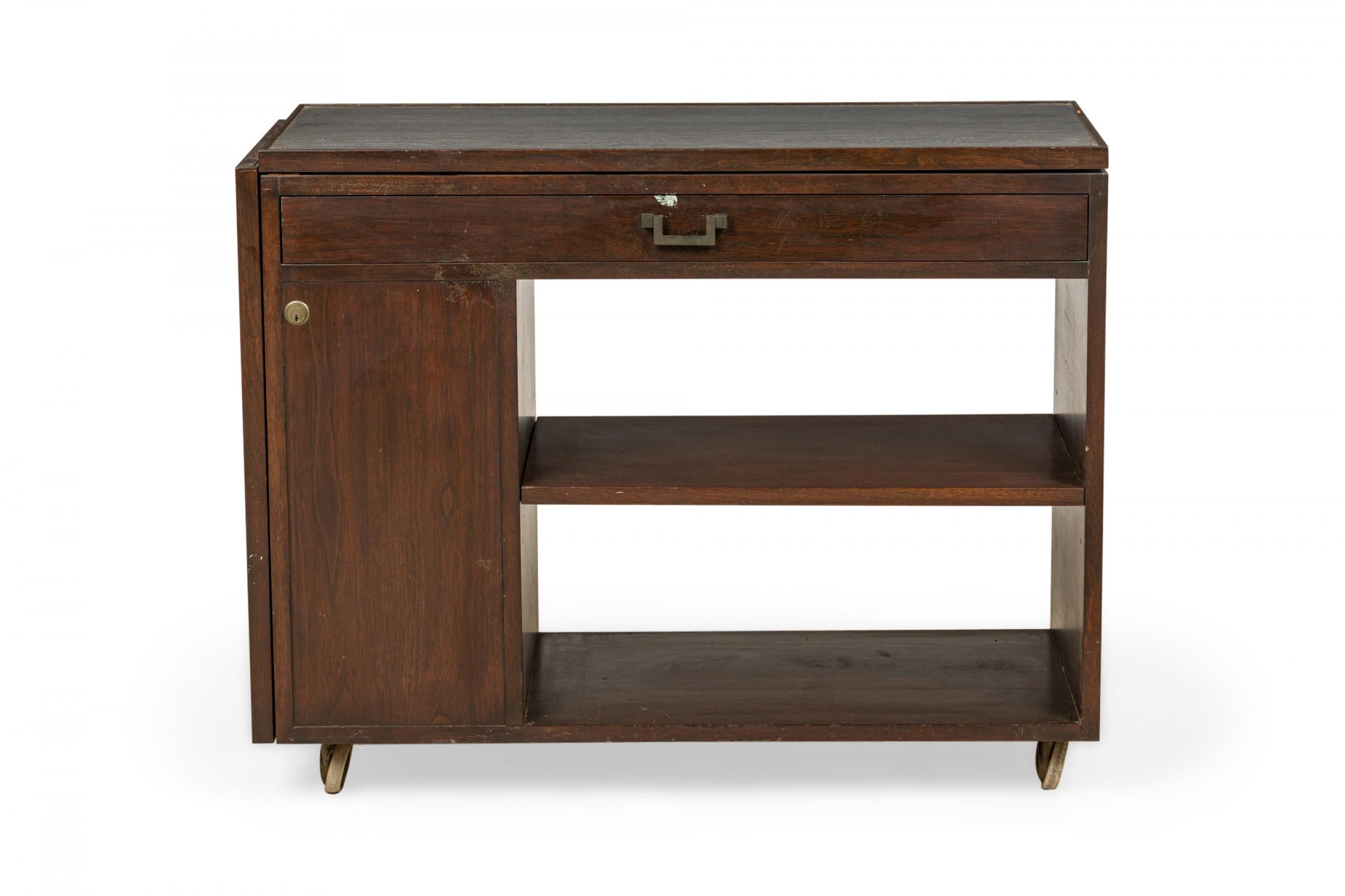 American Mid-Century rectangular serving trolley with a dark stained walnut frame, featuring a closed left side cabinet and two open shelves on the right below a drawer with bracket-shaped brass hardware, topped with an inset slate surface with a