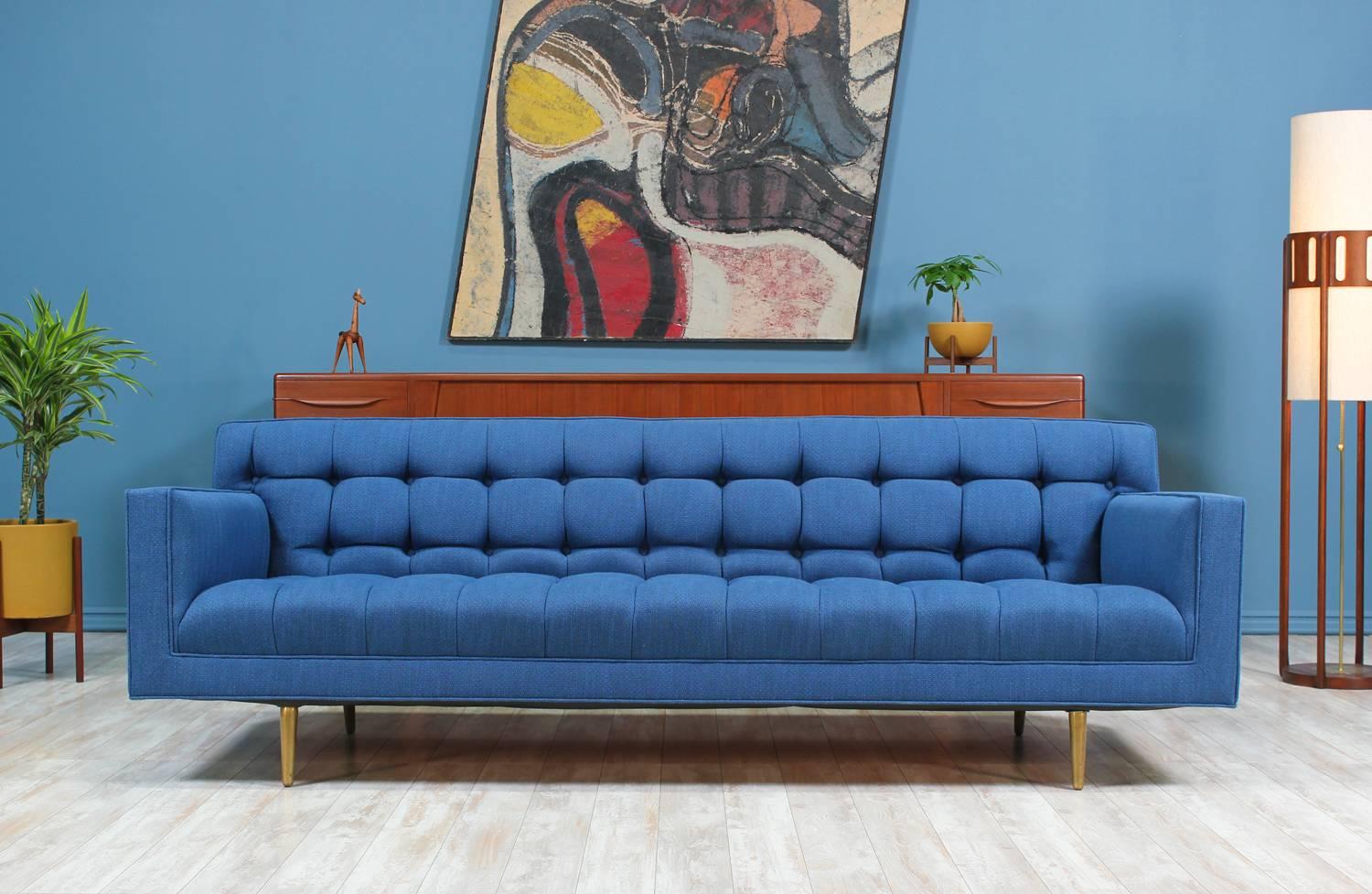 Mid Century Modern sofa designed by Edward J. Wormley for Dunbar in the United States circa 1950’s. This sofa features a beautiful biscuit tufted detail on the blueberry tweed fabric upholstery which is complimented with the elegant solid brass