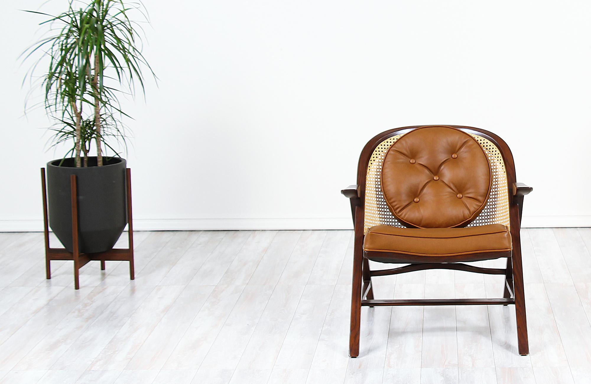 Iconic Model 5700-A lounge chair designed by Edward J. Wormley for Dunbar in the United States, circa 1950s. This rare design features a sturdily constructed walnut-stained oak wood frame with a newly woven cane backrest and new leather upholstery