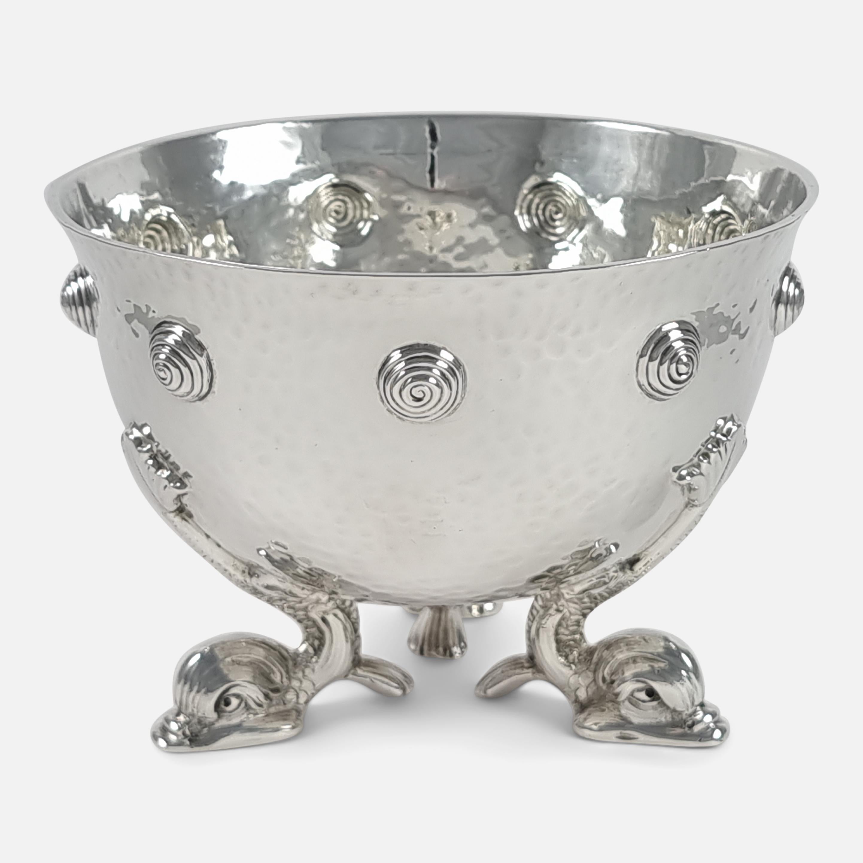 An Edward VII sterling silver Arts & Crafts style bowl by Mappin & Webb, London, 1906. The bowl is of circular form, with spot-hammered decoration, a band of punched spiral beads to the body, and sitting on three mythical dolphin feet.

Assay: -