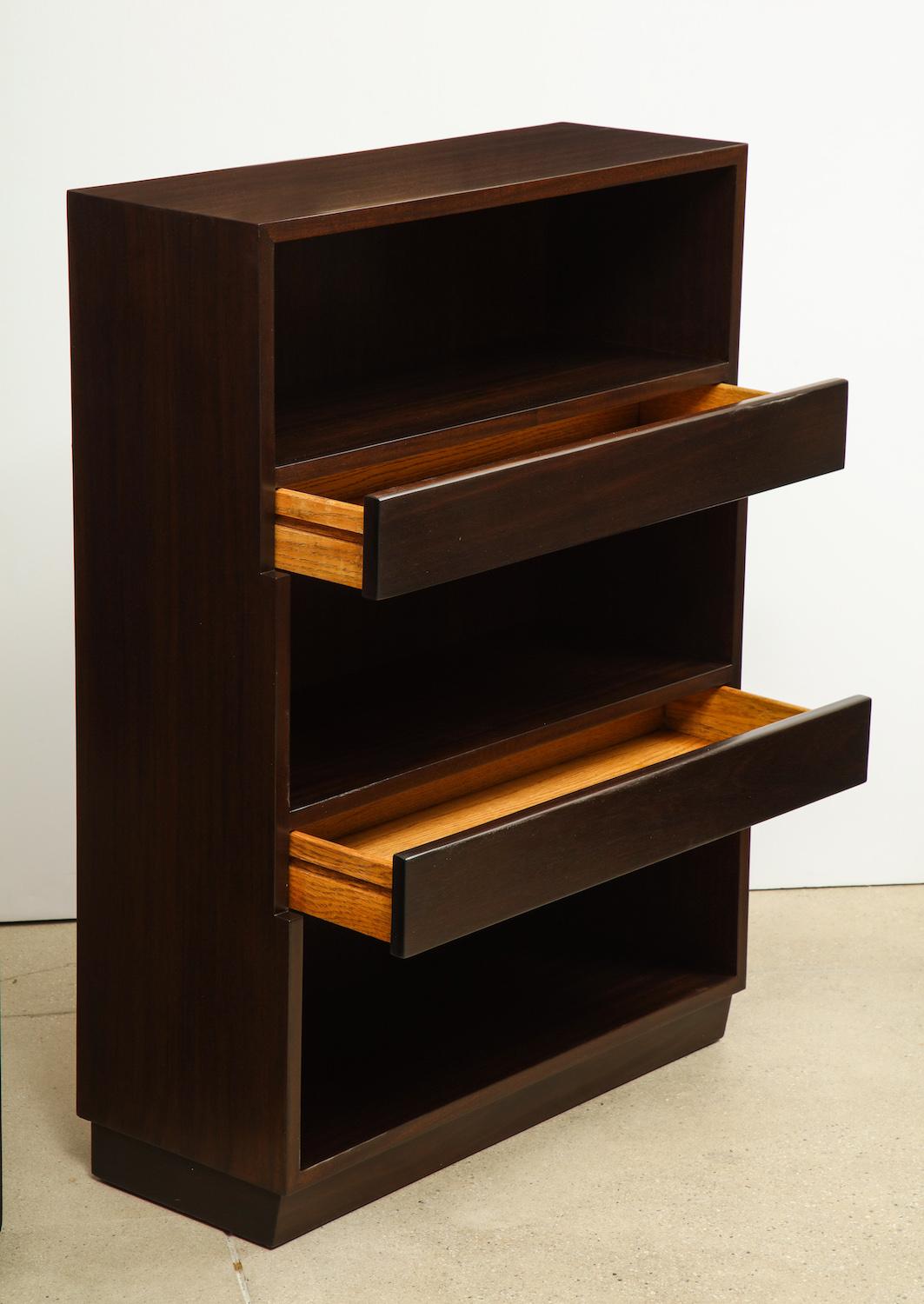 By Edward Wormley for Dunbar. Dark stained mahogany bookcases that step-up as they ascend. 2 drawers separate the three open storage areas. Each one is signed with the Dunbar label.
