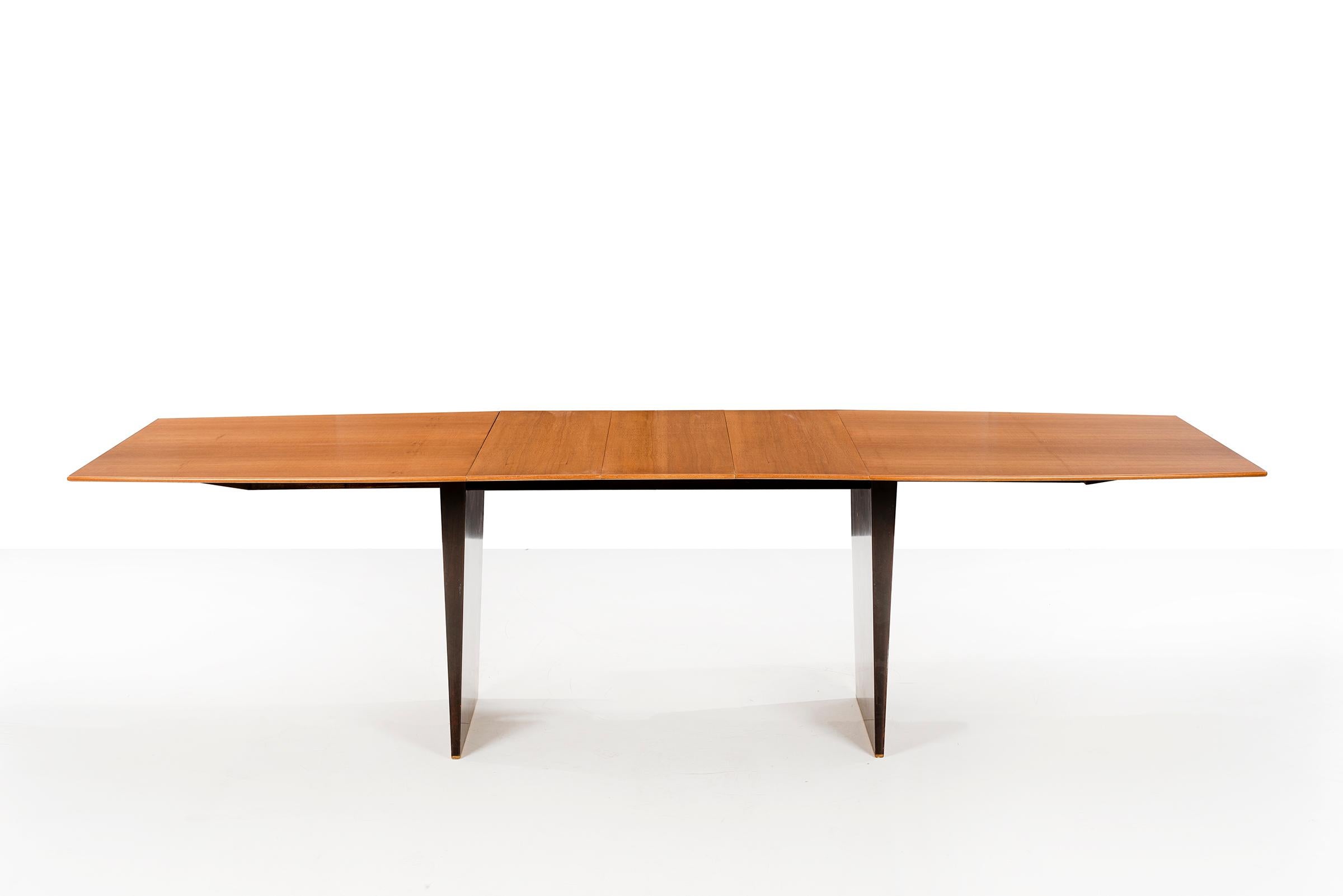 EDWARD WORMLEY (1907 - 1995)
Model no. 5640 Dining Table
Boat-shaped tawi wood dining table raised on a pair of wide tapering mahogany legs with brass sabots.
 Featuring 3, 12 inch leaves in opposing grainwork. The table is 108 inches when fully