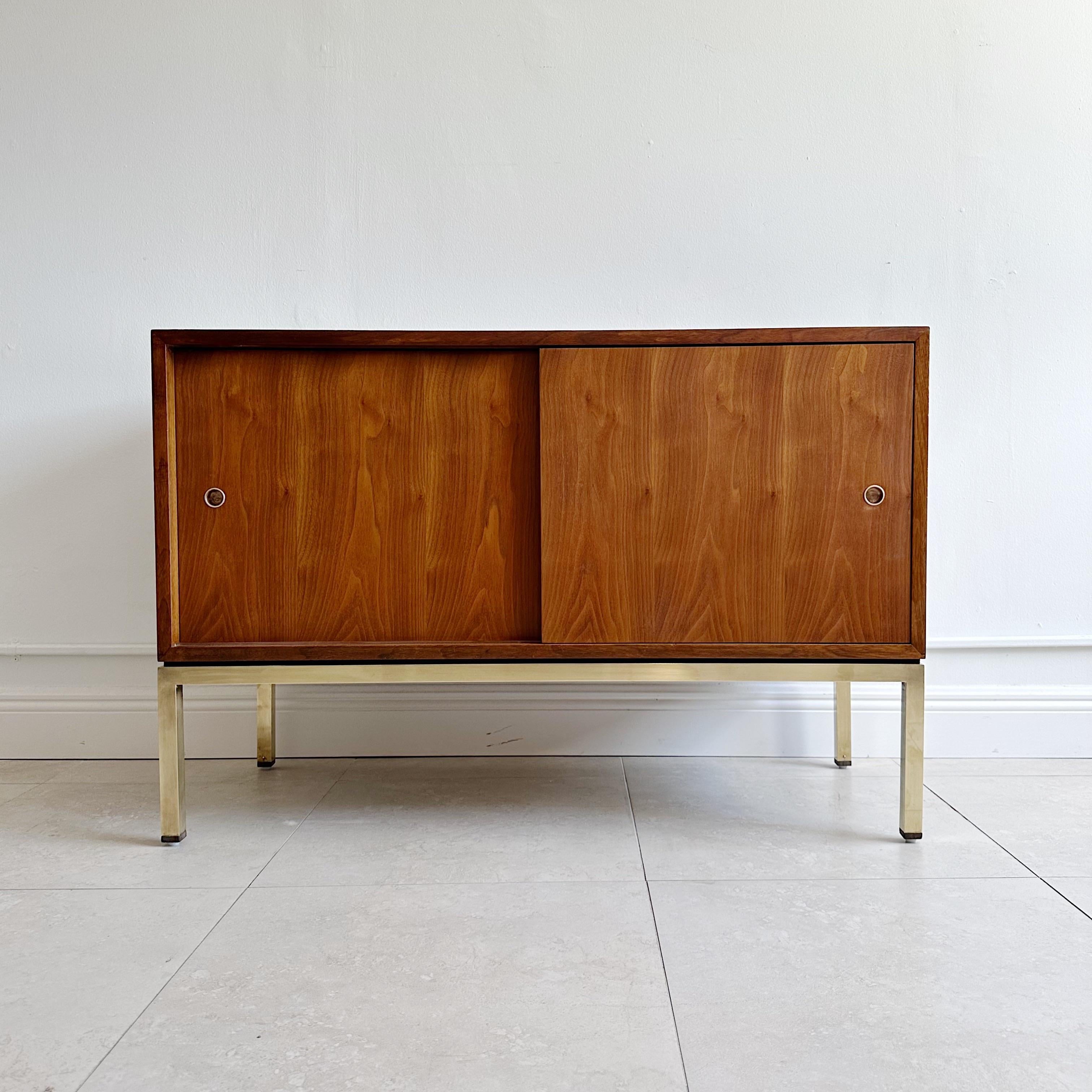 Edward Wormley solid walnut cased cabinet with two sliding doors supported on four legged brass frame with walnut caps on the feet. Original Dunbar label on the back. 