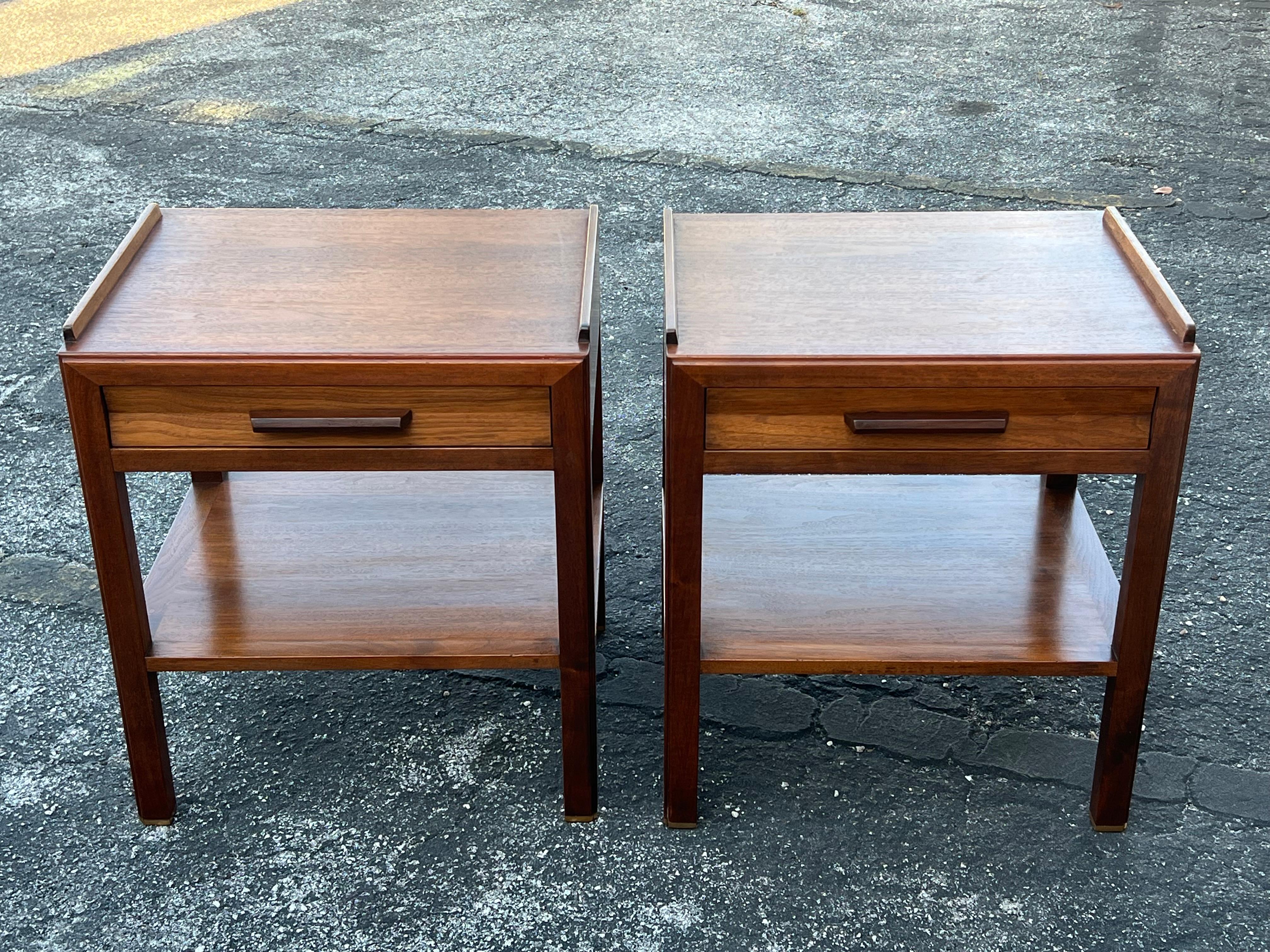 A pair of classic night stands by Edward Wormley for Dunbar. Single drawer with lower shelf, quality walnut construction, rosewood handles, solid brass gliders. The backs are finished. These practical night stands are modern yet can also work in a
