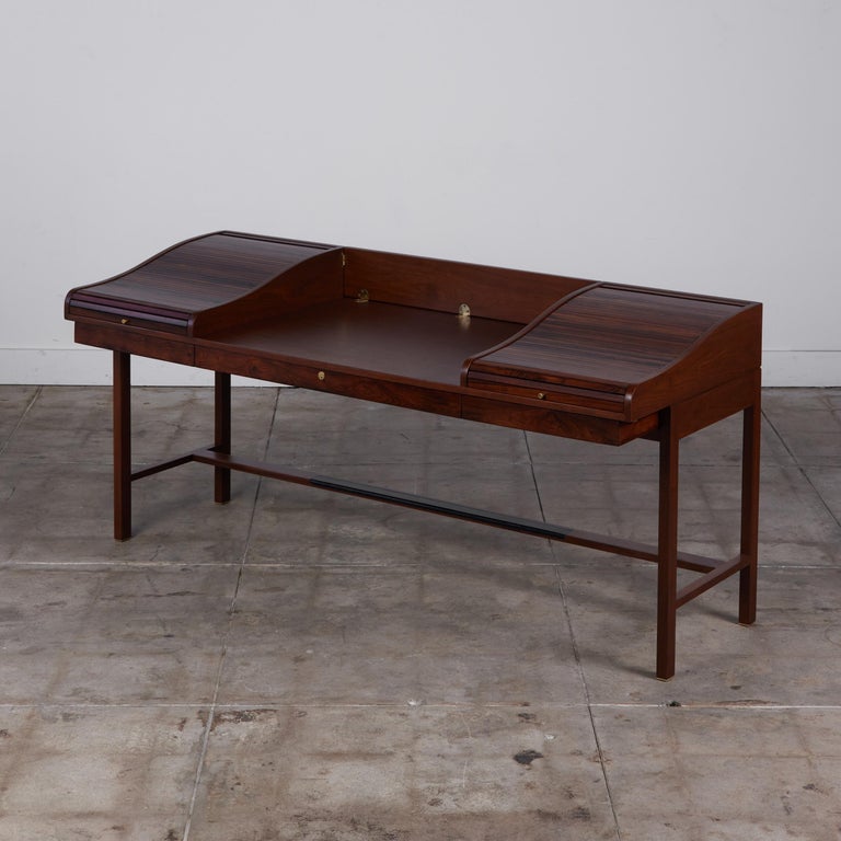 Rosewood executive desk by Edward Wormley c.1950s, USA, for Dunbar. The desk has three shallow drawers that run the length of the desk. The top of the desk features two roll top tambour doors which flank each side of the piece. Once opened, the