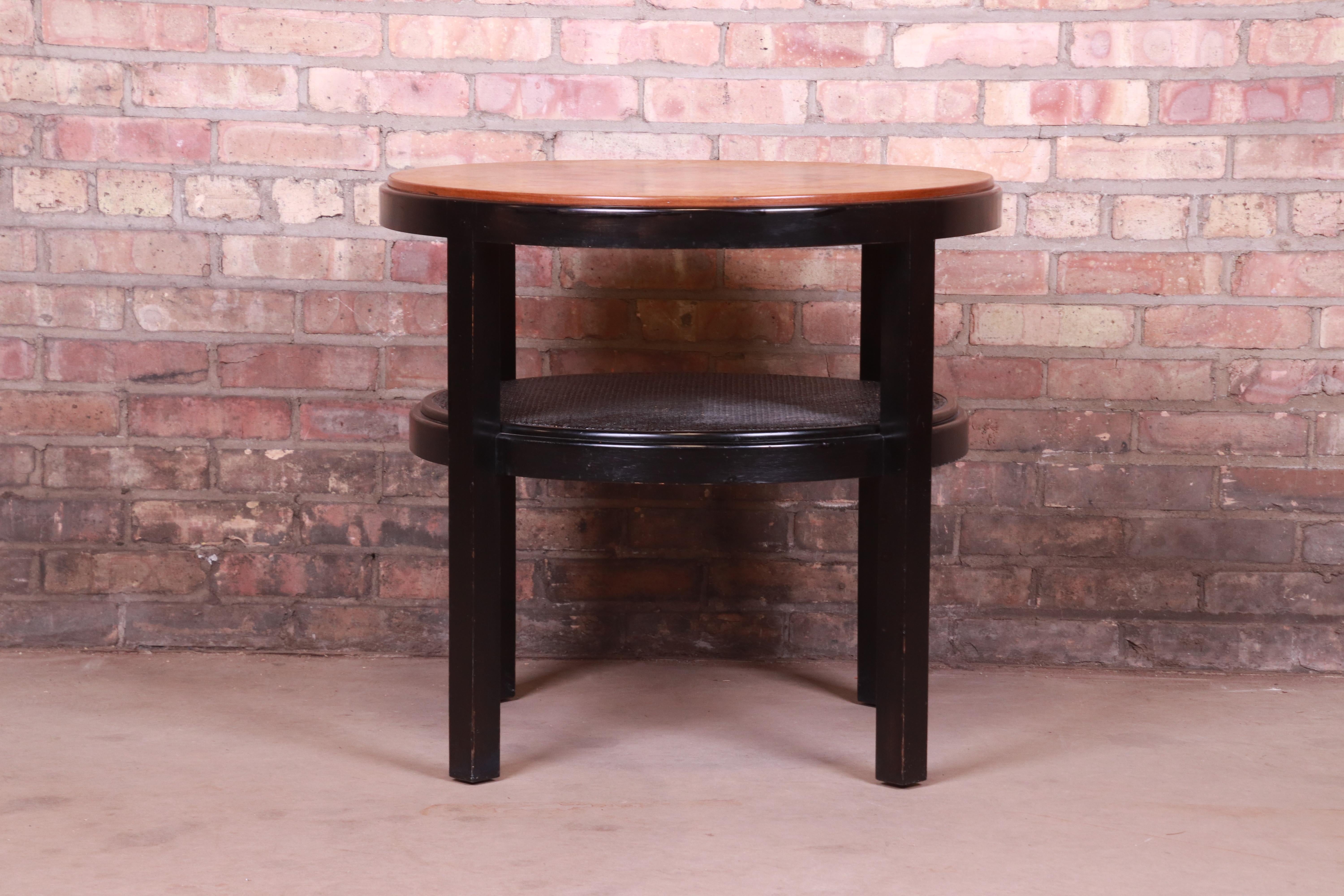 A gorgeous Mid-Century Modern two-tier tea table or occasional side table

By Edward Wormley for Dunbar

USA, circa 1960s

Book-matched burled olive wood top, with ebonized frame and caned lower shelf.

Measures: 28
