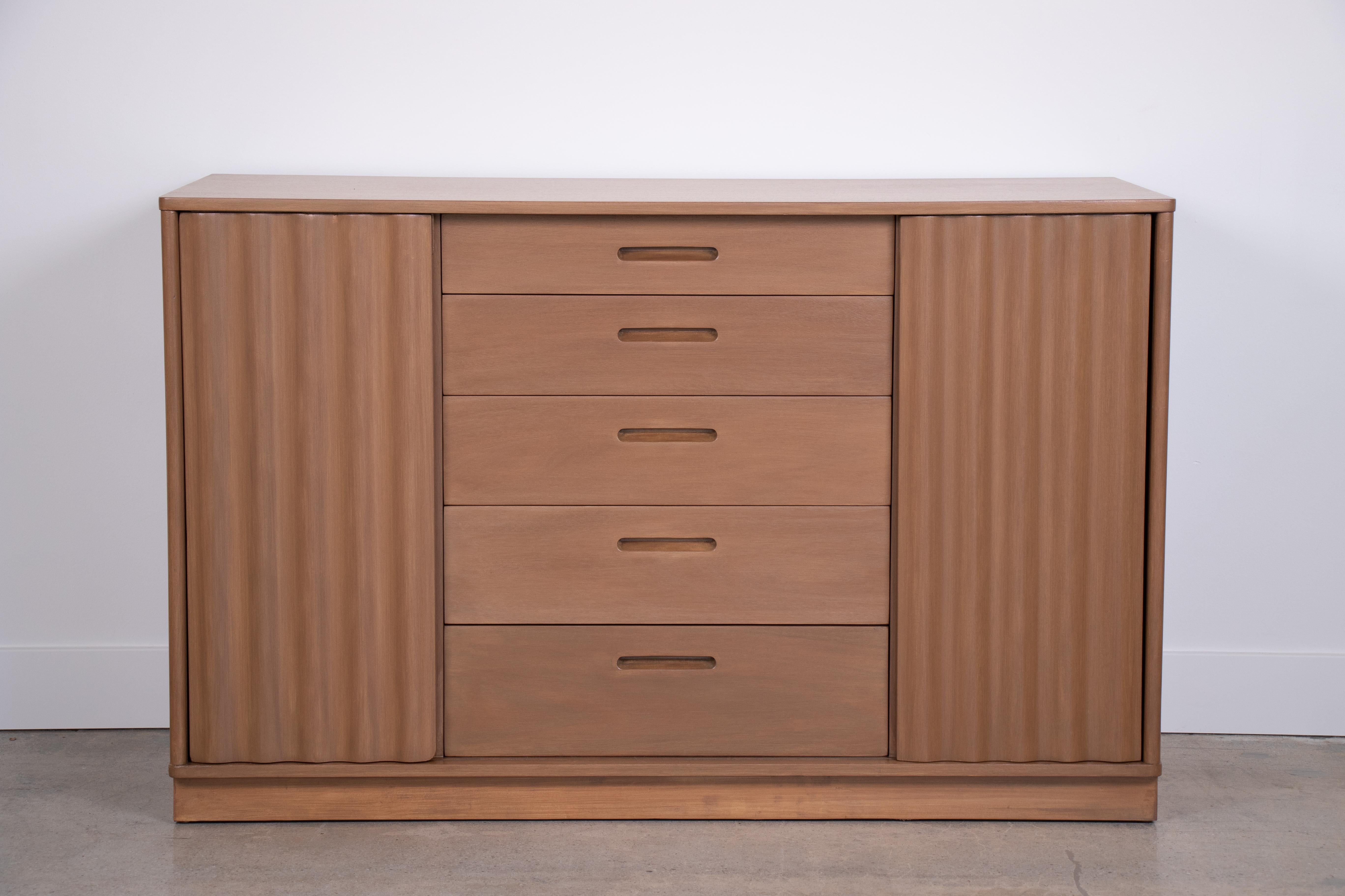 Edward Wormley for Dunbar cabinet. Beautiful sliding wavy front doors and 5 center drawers with side shelving. Newly refinished. Dunbar tag inside drawer.