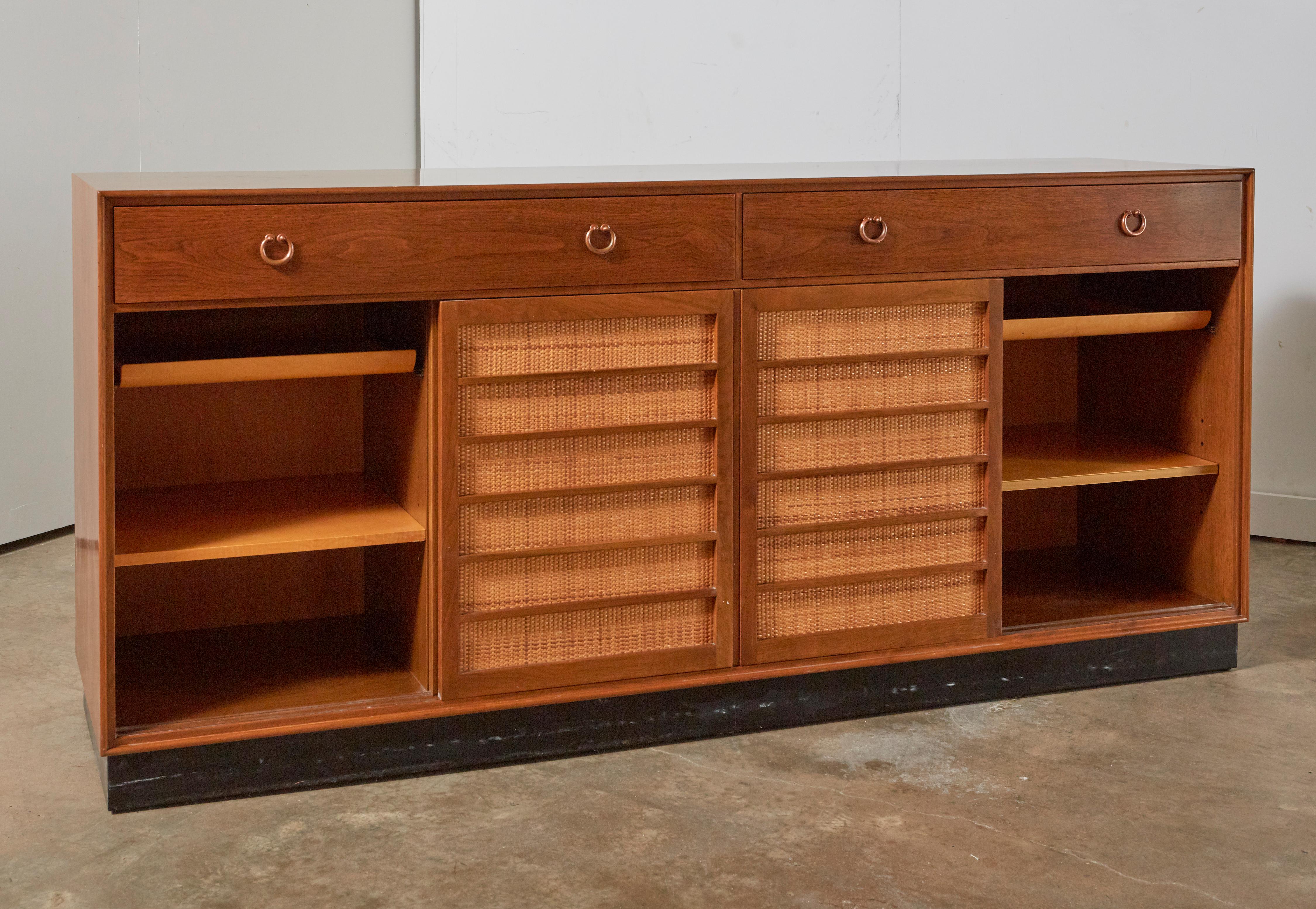 A mahogany and cane fronted sliding door credenza by Ed Wormley for Dunbar. Excellent vintage condition with elegantly caned panel sliding doors showing little to no wear, and boasting unusual copper hanging ring pulls. Two drawers at top with four