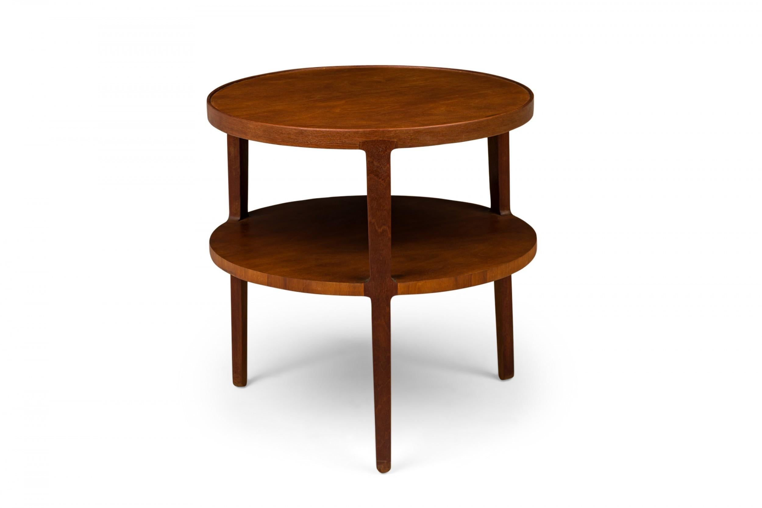 American mid-century two-tier end / side table with a circular top above a circular stretcher shelf supported by three tapered legs, finished in walnut veneer. (EDWARD WORMLEY FOR DUNBAR FURNITURE COMPANY)