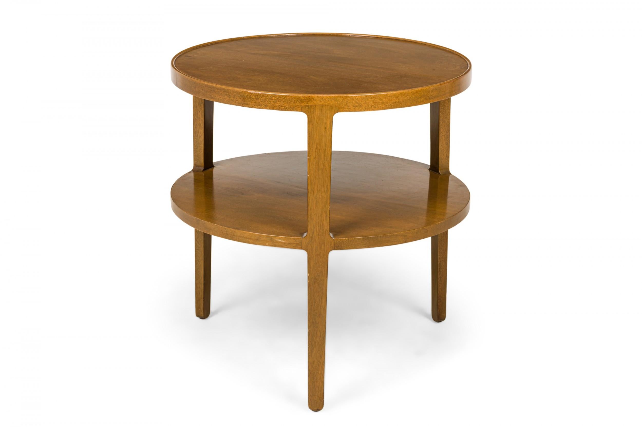 American mid-century circular wooden end / side table with a circular top with shallow lip above an identical stretcher shelf supported on the exterior by three tapered square legs. (EDWARD WORMLEY FOR DUNBAR FURNITURE COMPANY)