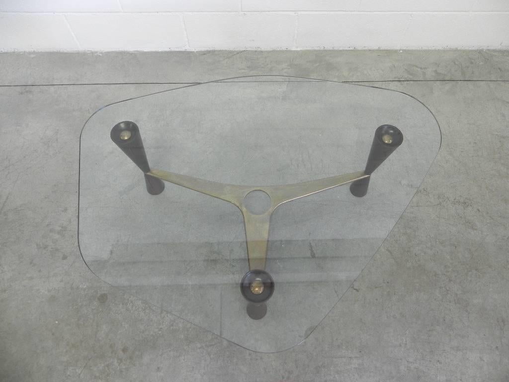 Asymmetrical Edward Wormley for Dunbar coffee table rounded beveled top on three conoid legs by a curvilinear brass stretcher, flaking to glass around.