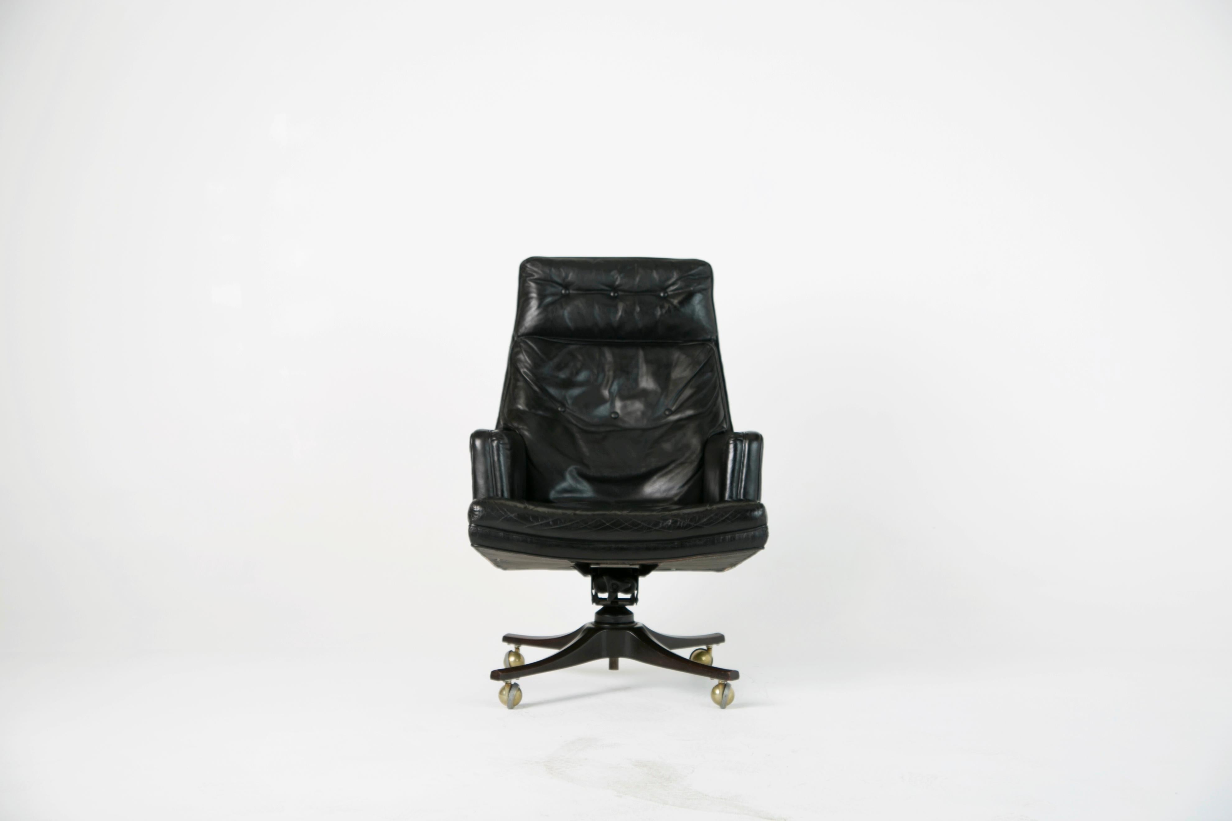 For the Executive with panache, this sizable black leather desk chair was designed by Edward Wormley and produced by Dunbar in the 1960s. This earlier production example has a sculpted wooden base rather than the later metal bases. Signed on the