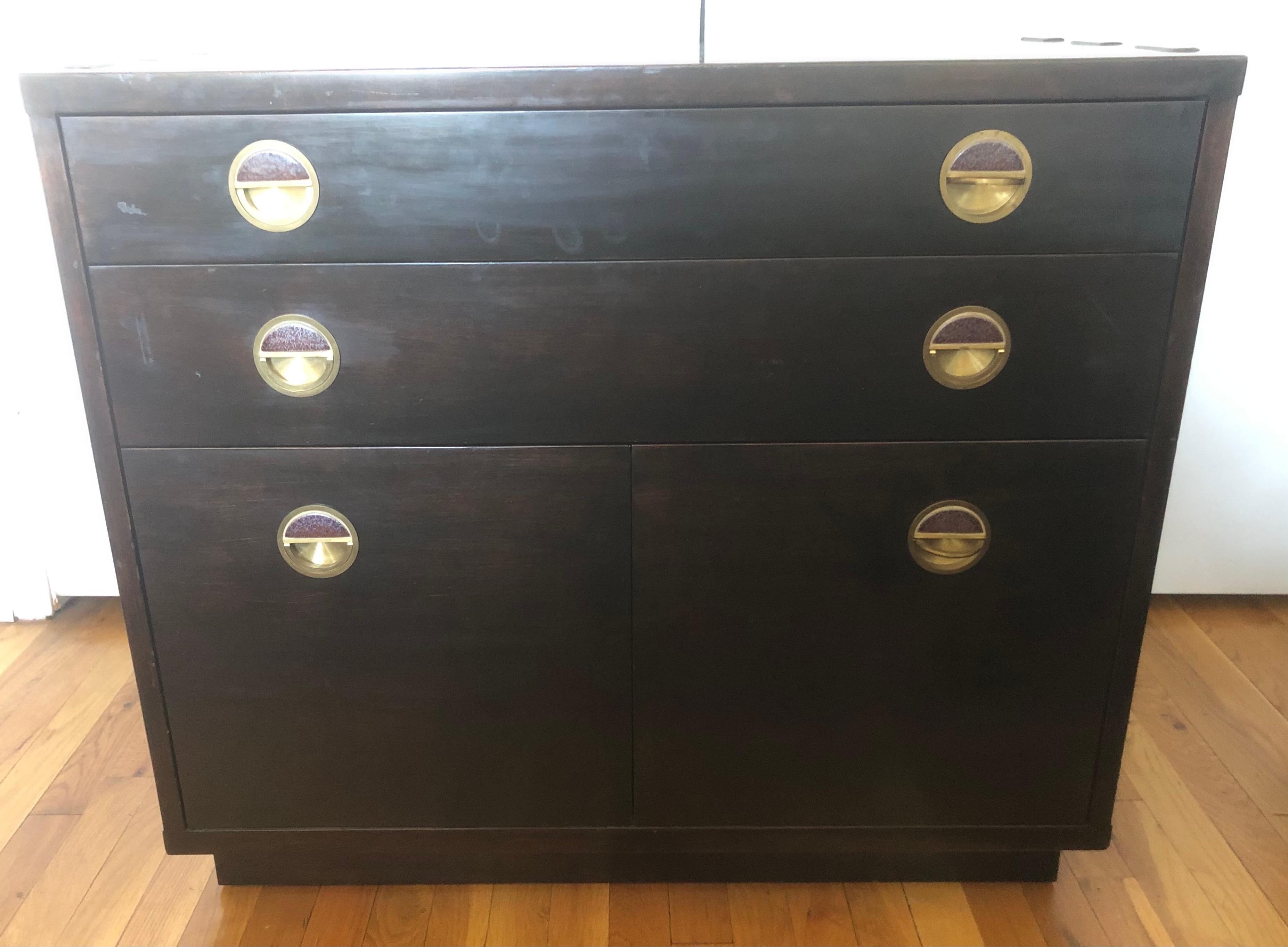 Model 5770 Janus Collection chest of drawers featuring brass pulls with inset purple-blue demi-lune Natzler ceramic tiles, and exaggerated dovetail knuckle joints on tops, sides, and bottom. 

The dark stained mahogany case is set with two shallow