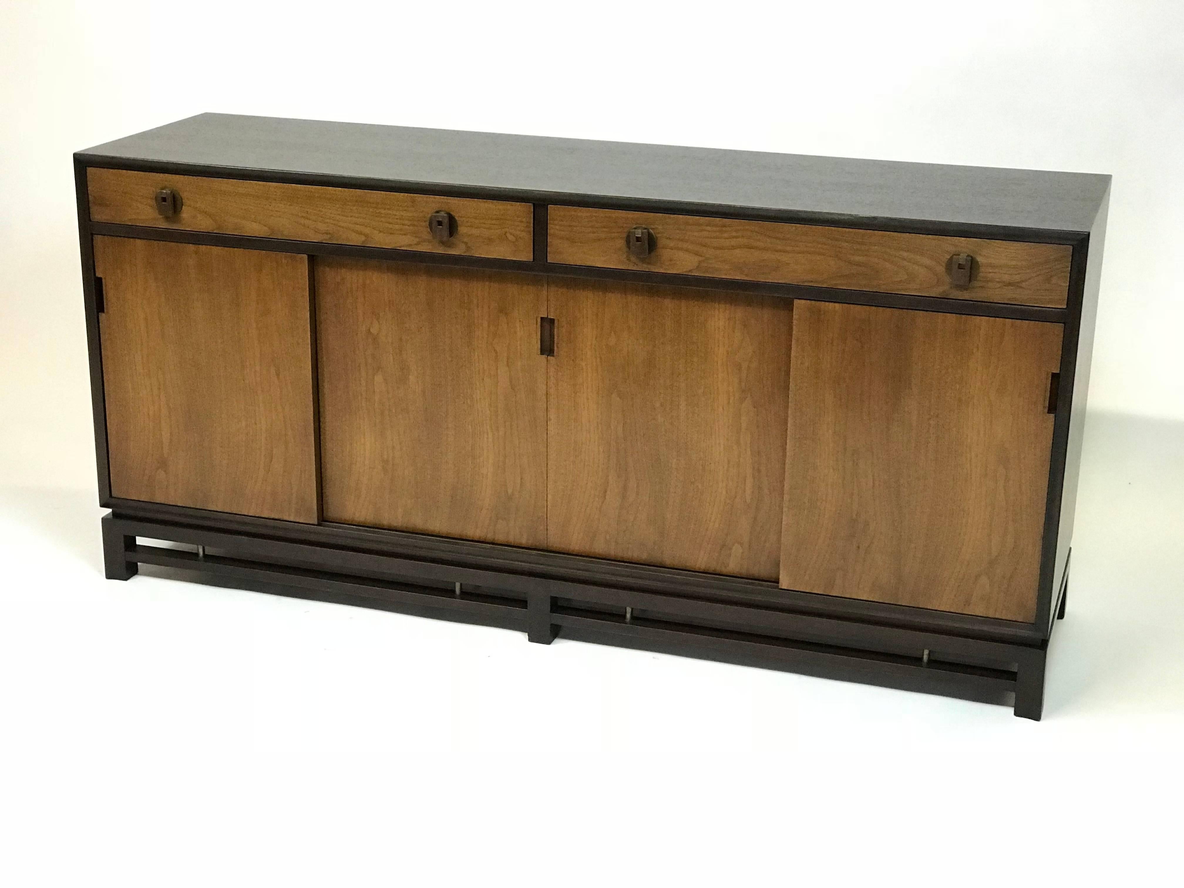Mid-Century Modern, two-tone, sideboard or credenza by Edward Wormley for Dunbar features an ebonized mahogany surround with walnut doors and brass handles and accents on the lattice base. The cabinet has a finished backside.