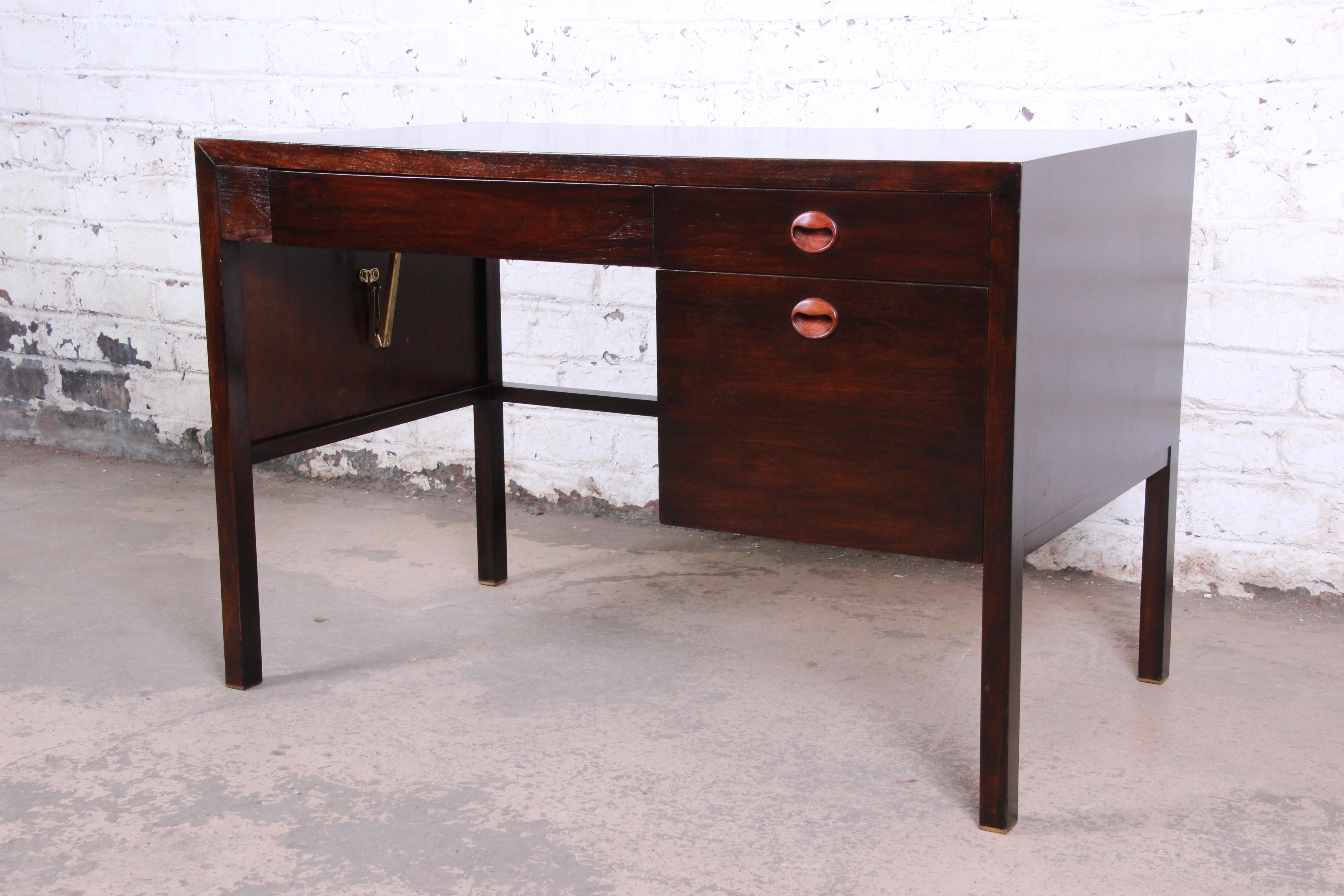 An exceptional Mid-Century Modern drop-leaf desk designed by Edward Wormley for Dunbar. The desk features rich mahogany wood grain with carved rosewood drawer pulls. It offers good storage, with three drawers. The desk has a unique design, with a