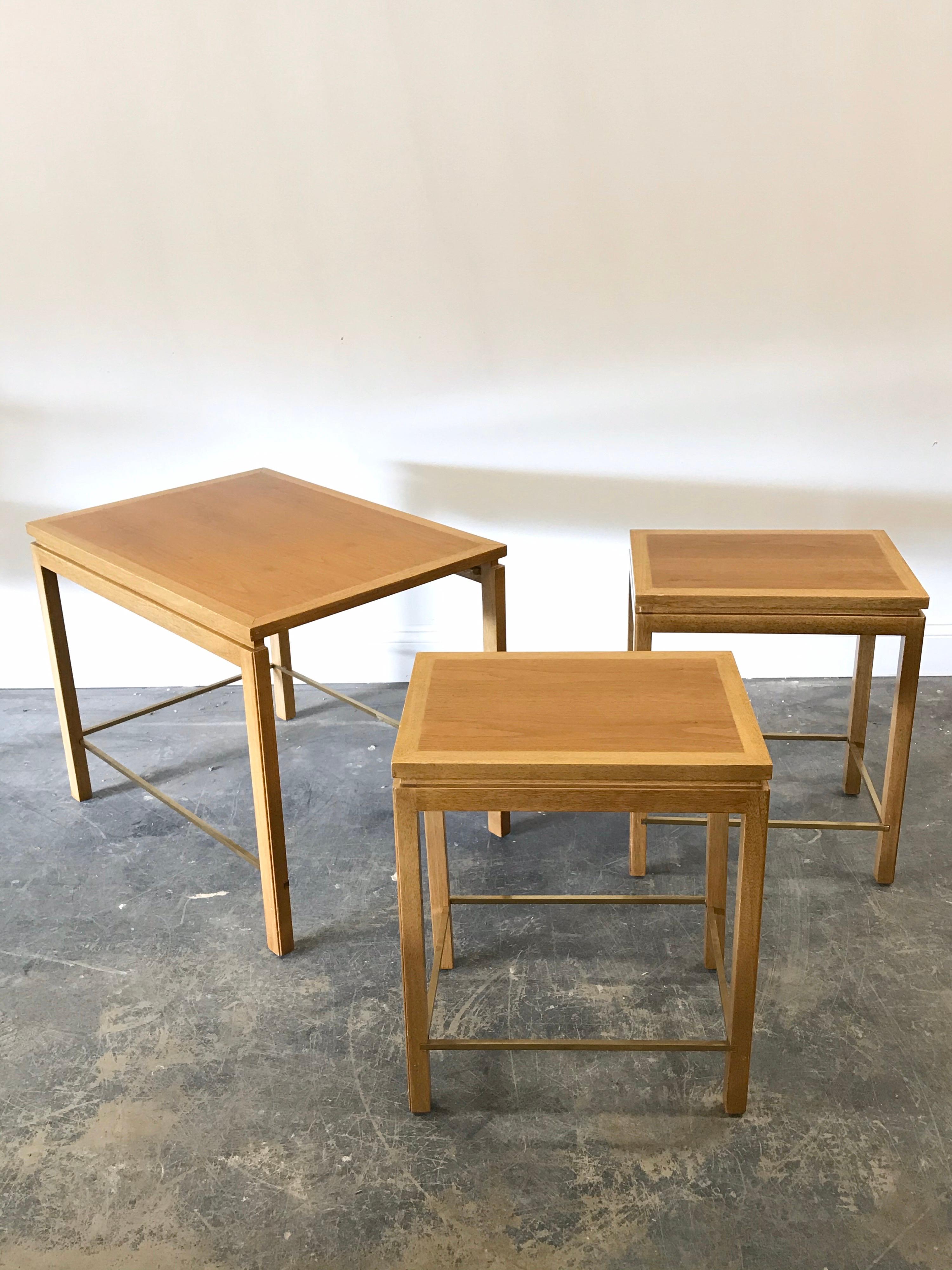 Beautiful set of three nesting tables designed by Edward Wormley for Dunbar. Tables features a mahogany structure and banding, with a soft walnut top, and finished off with brass stretchers. Please note the listed size is the larger table, the