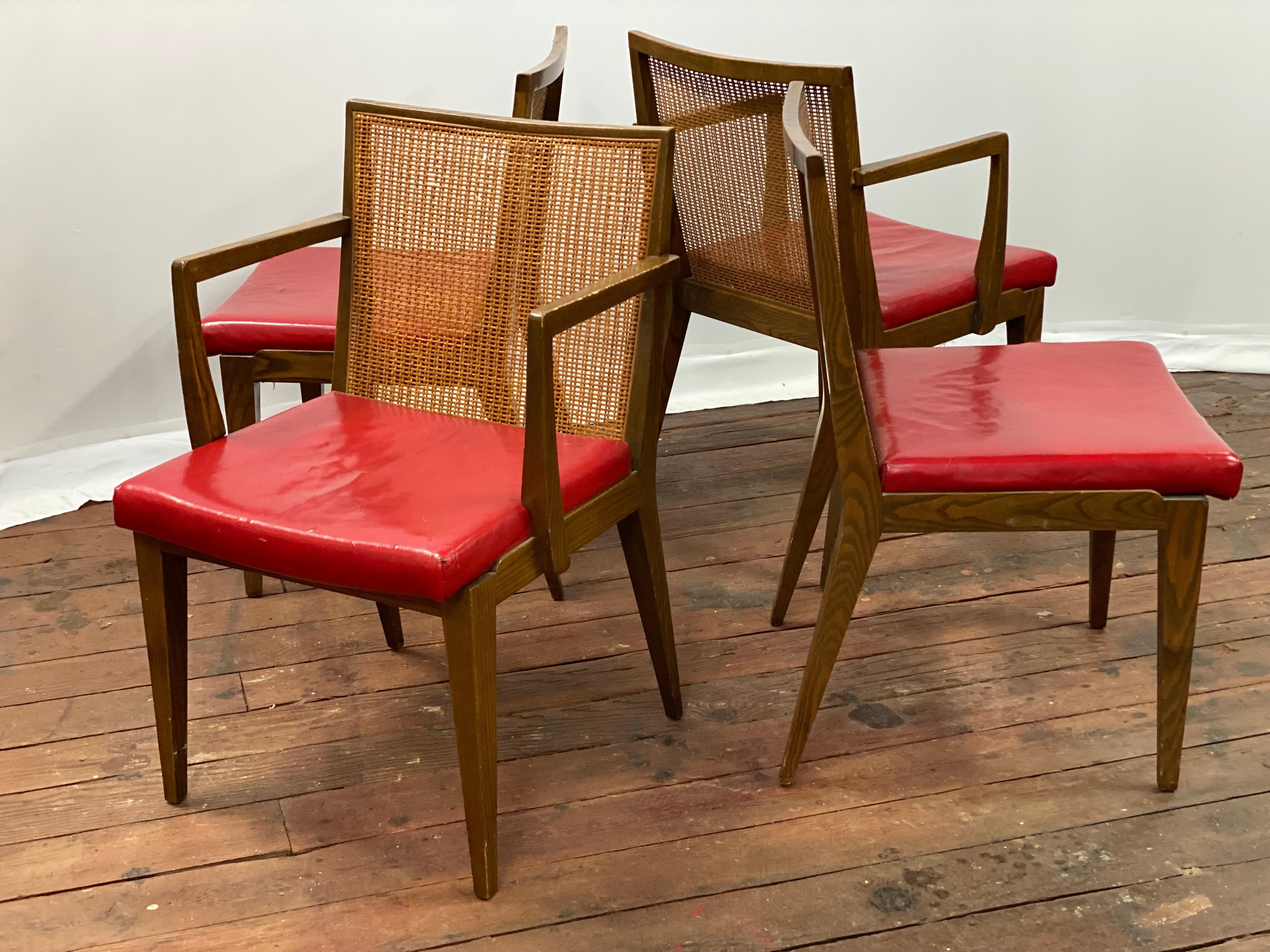 A set of four distinct oak and cane back dining chairs designed by Edward Wormley for Dunbar, Berne, Indiana. Each chair still retains the gold metal tag on the underside of each seat. Solid oak frames, tapered legs and caned backs. Bright candy