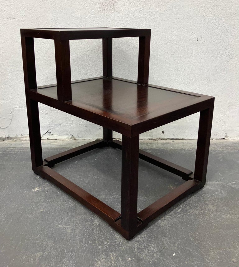 An early example of Edward Wormley's sophisticated Modernism. Stepped two-tier end tables with subtle Chinoise elements to the carving of the base. These retain the original dark mahogany stain, which is very nicely preserved and shows a rich warm