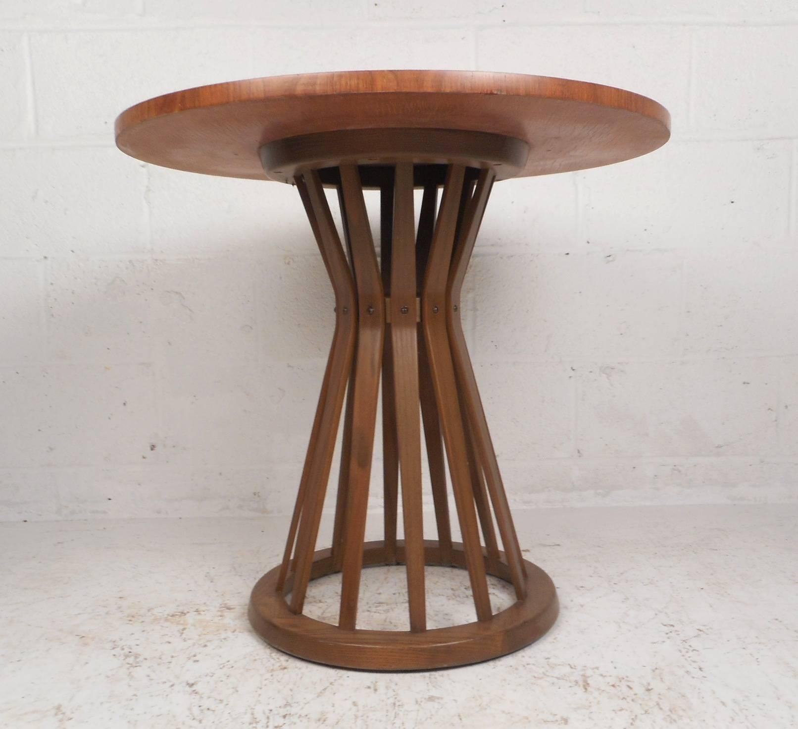 This iconic Mid-Century Modern side table by Edward Wormley features a gorgeous round top with walnut wood grain. This unique piece has an hourglass shaped base with spindles tapering down to a circular bottom. This stylish vintage modern end table