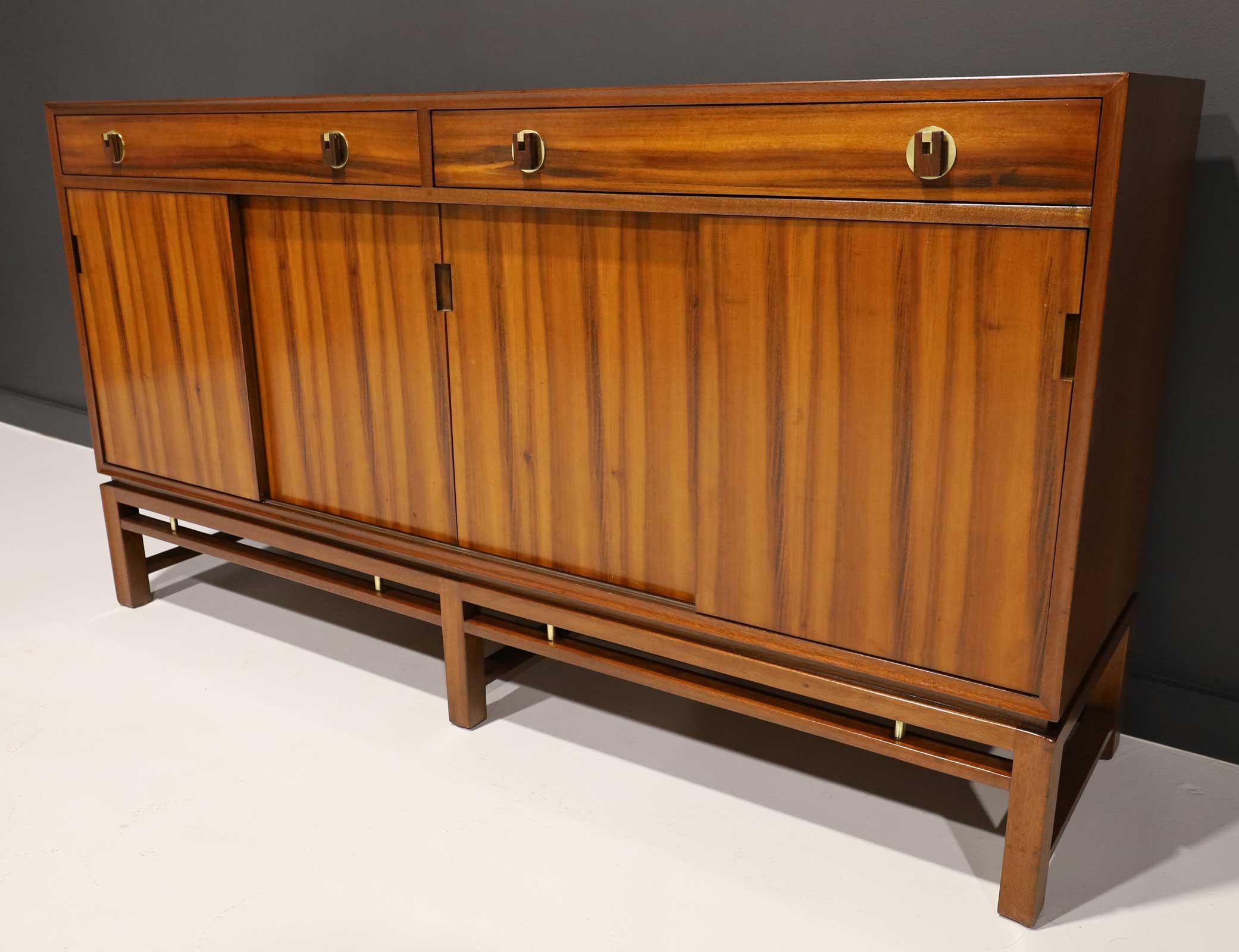 Not often seen, a fully restored sliding door sideboard by Edward Wormley for Dunbar. The cabinet features four sliding doors with loads of interior storage. The top section has two drawers each with two brass and wood decorative knobs. Brass trim