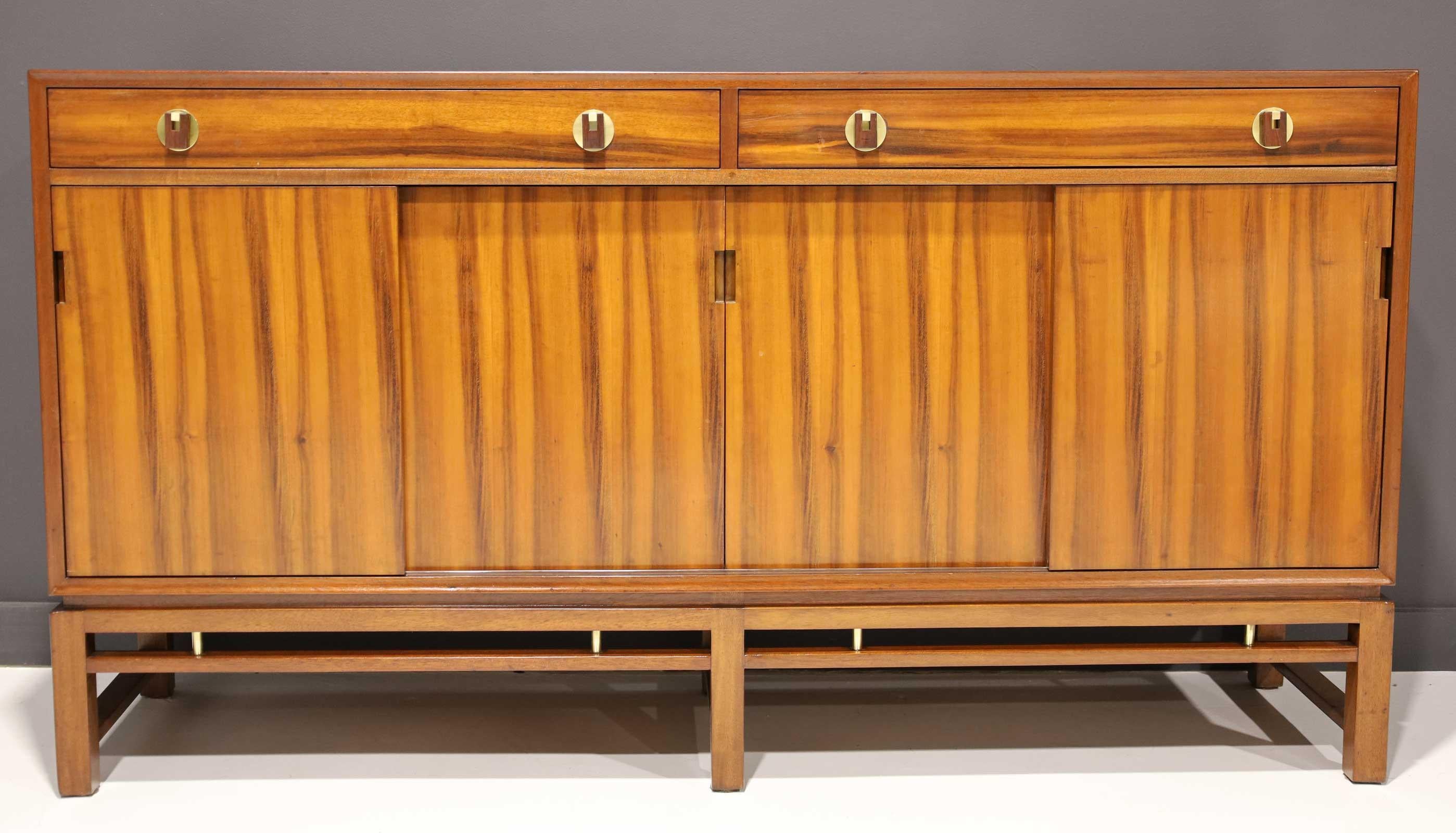Not often seen, a fully restored sliding door sideboard by Edward Wormley for Dunbar. The cabinet features four sliding doors with loads of interior storage. The top section has two drawers each with two brass and wood decorative knobs. Brass trim