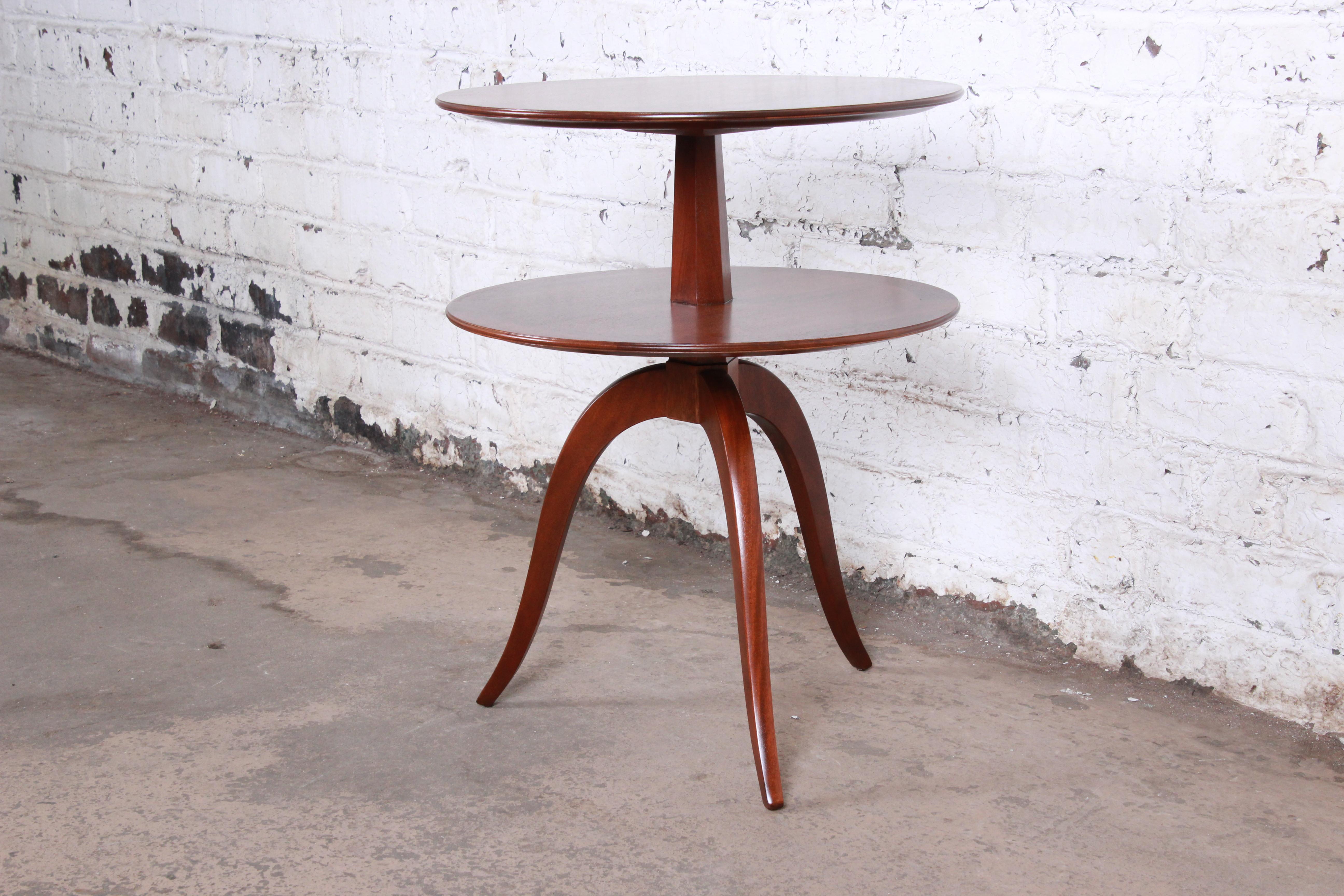 A rare and exceptional two-tiered round side table by Edward Wormley for Dunbar Furniture, circa 1940s. The table features stunning mahogany wood grain with a round pedestal top and tripod splayed leg base. The original early Dunbar label is