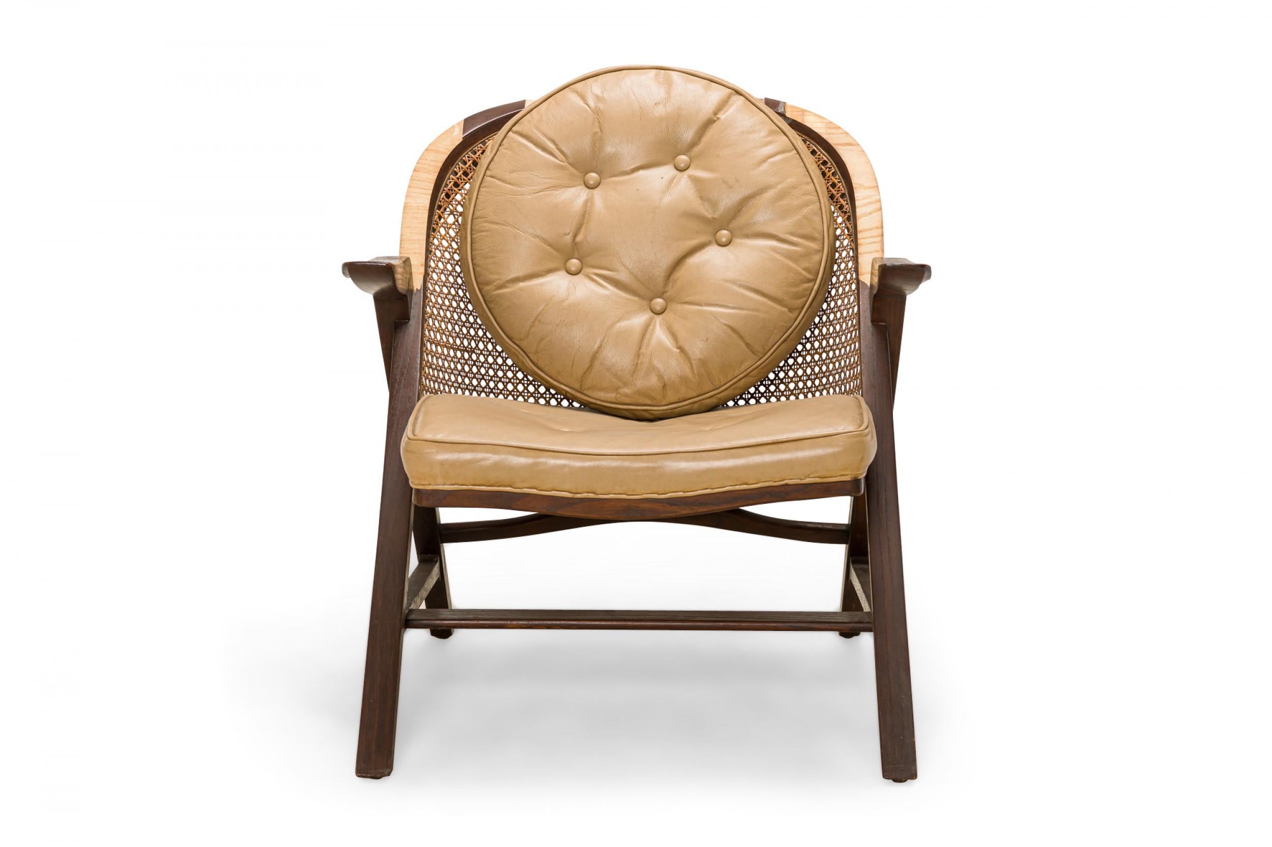 American Mid-Century 'Janus' lounge / armchair with a wooden frame with dark walnut veneer, a rounded caned back, and a tan leather button tufted seat cushion and round back cushion, resting on four angled square walnut legs. (EDWARD J WORMLEY FOR
