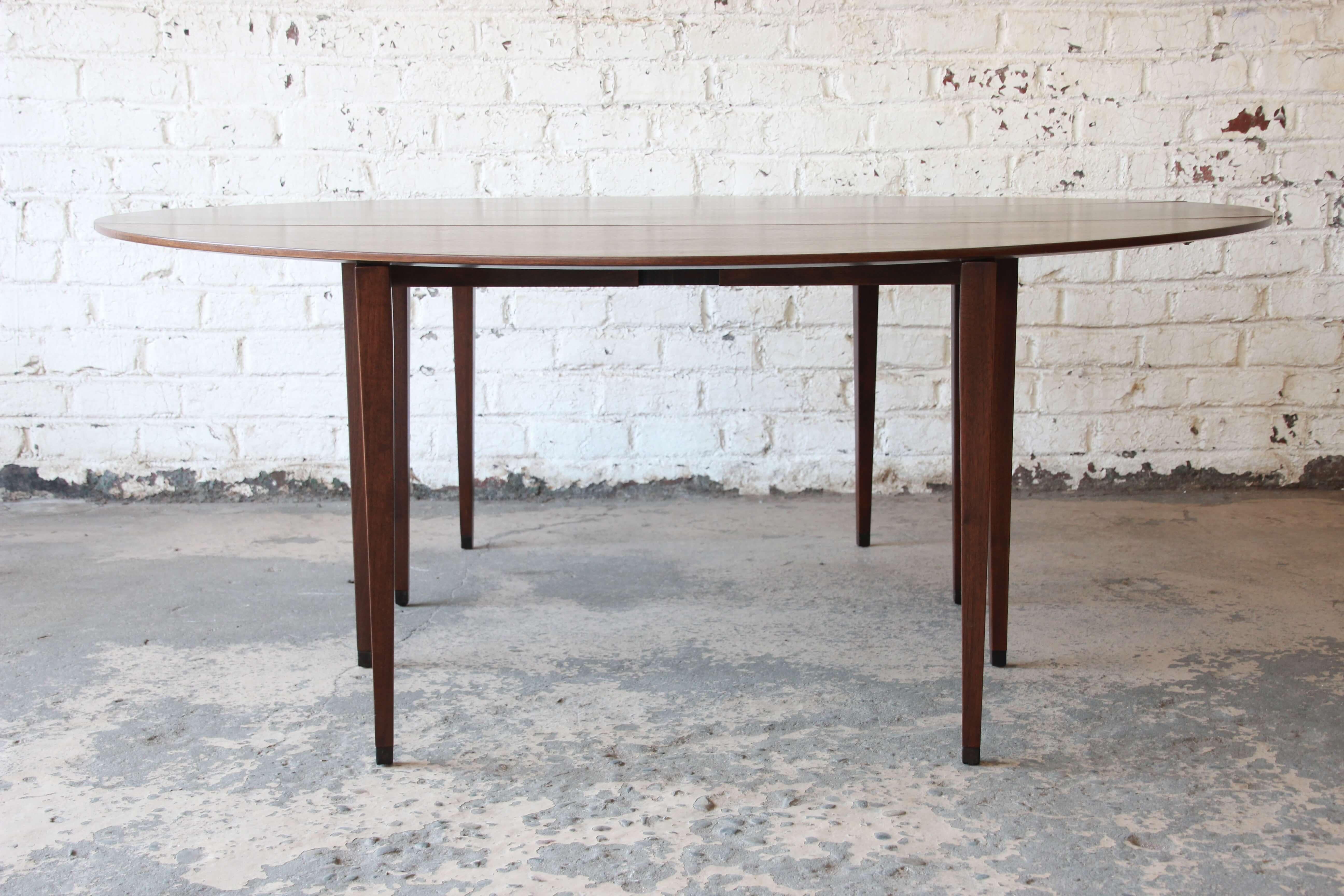 Offering a very nice Edward Wormley for Dunbar walnut oval drop-leaf dining table. The table has a beautiful bookmatched walnut wood grain. The table can be use as a nice sofa back table and then also extends to 72