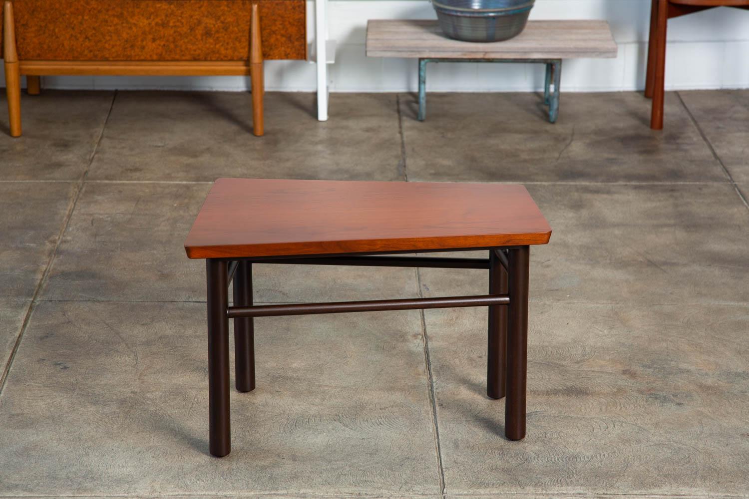 A wedge shaped side table by Edward Wormley for Dunbar. This end table features a trapezoidal walnut top, which sits atop dark contrasting mahogany legs with angled horizontal stretchers. Retains original [ Dunbar - Berne, Indiana] metal label on