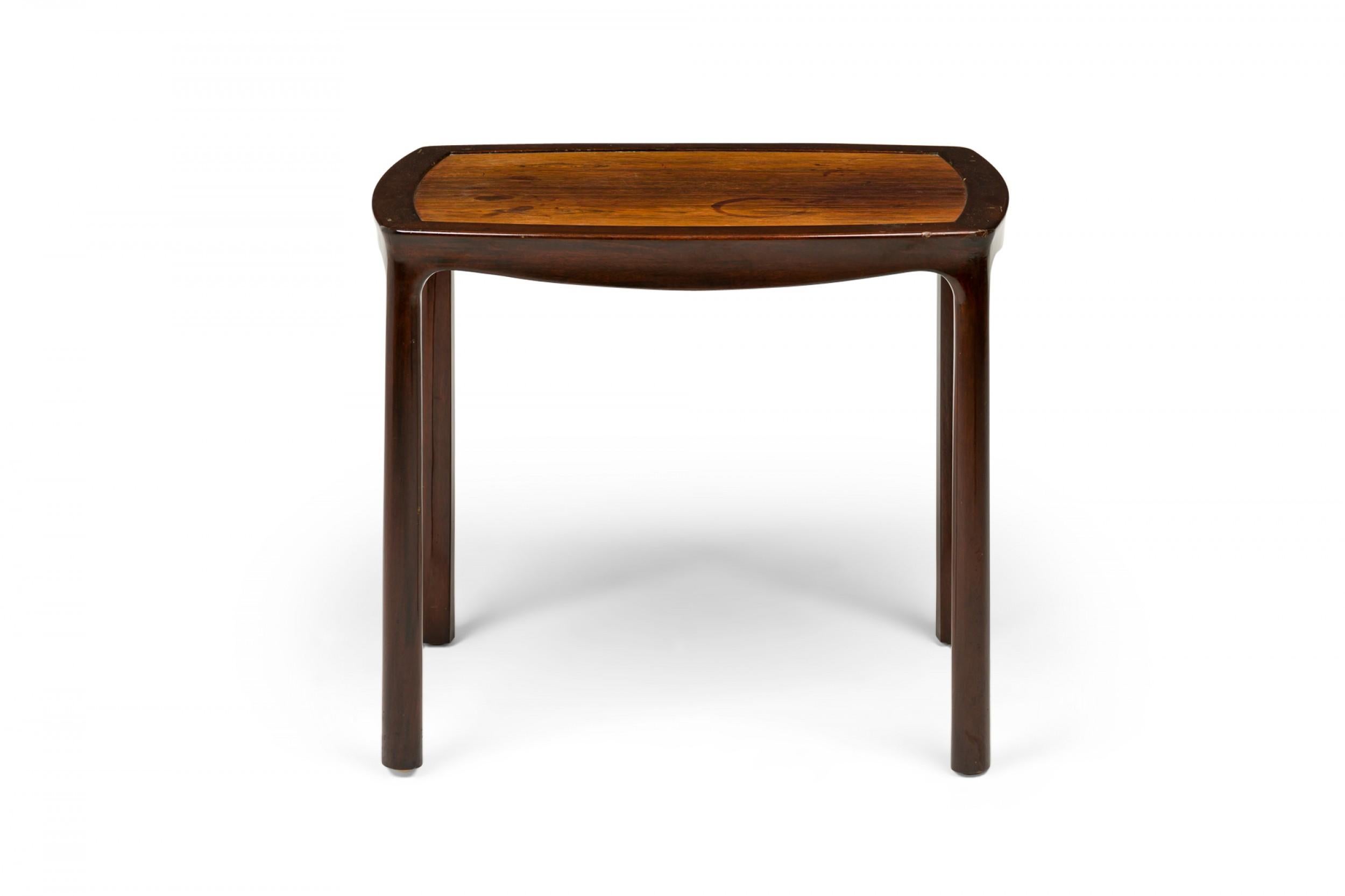 American mid-century end / side table with a slightly rounded rectangular top with a lighter stained wooden inset top supported by a darker wooden frame with a shaped apron with four rounded legs. (Edward Wormley for Dunbar Furniture
