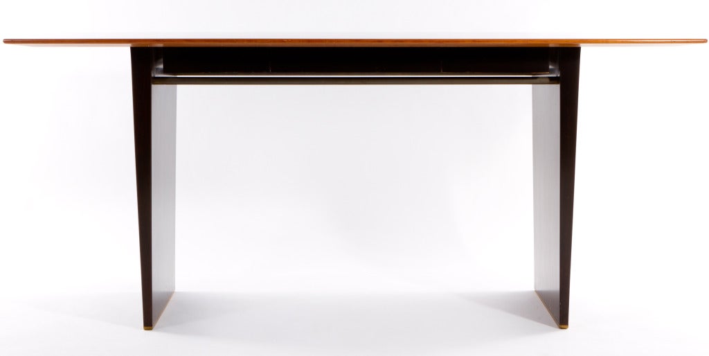 Elegantly shaped writing table designed by Wormley and manufactured by Dunbar. Tawi wood top and tapered mahogany legs with brass stretchers. Desk has 3 drawers. With label and original drop tag.