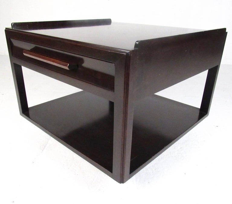 This stylish Mid-Century Modern Dunbar lamp table features rich mahogany finish, dovetailed drawers, and uniquely sculpted single drawer design. Unique drawer pull and raised edge style add to the Edward Wormley appeal of this vintage side table,