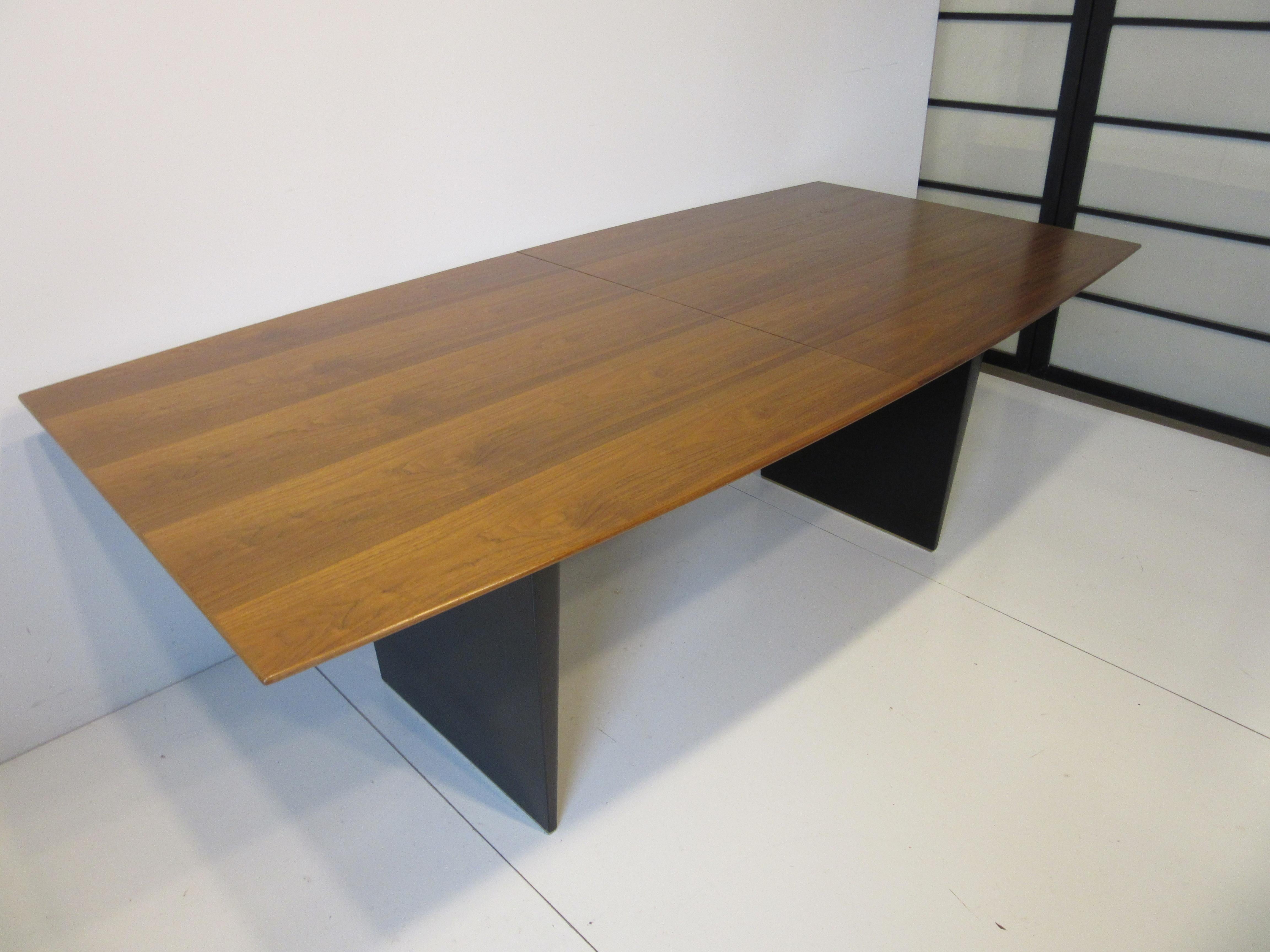 One of the best forms that came from the iconic mid century designer Edward Wormley, this walnut dining table with tapered ends to the top and wonderful graining has ebony toned plinth bases and brass shoes or feet. Well crafted mostly by hand from