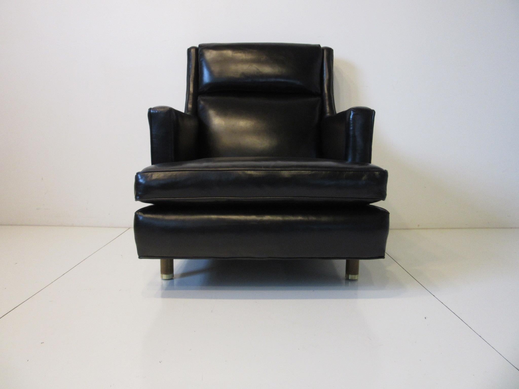 A high back well tailored lounge chair in black leather by the Dunbar Furniture company known for using the best materials and construction methods. Sitting on solid centrical mahogany legs with brass capped feet having springs to the seat bottom of