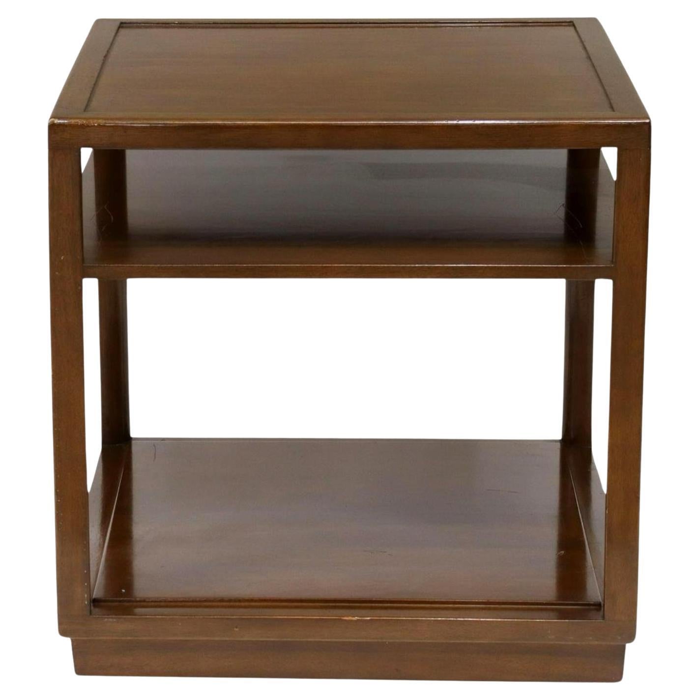 A single end table by Edward Wormley for Dunbar with square top and a fixed  shelf rising on plinth base.

USA, circa 1940-1950.

Signed with burnished Dunbar name and paper tag to underside.

Model #4776, in Amber wood