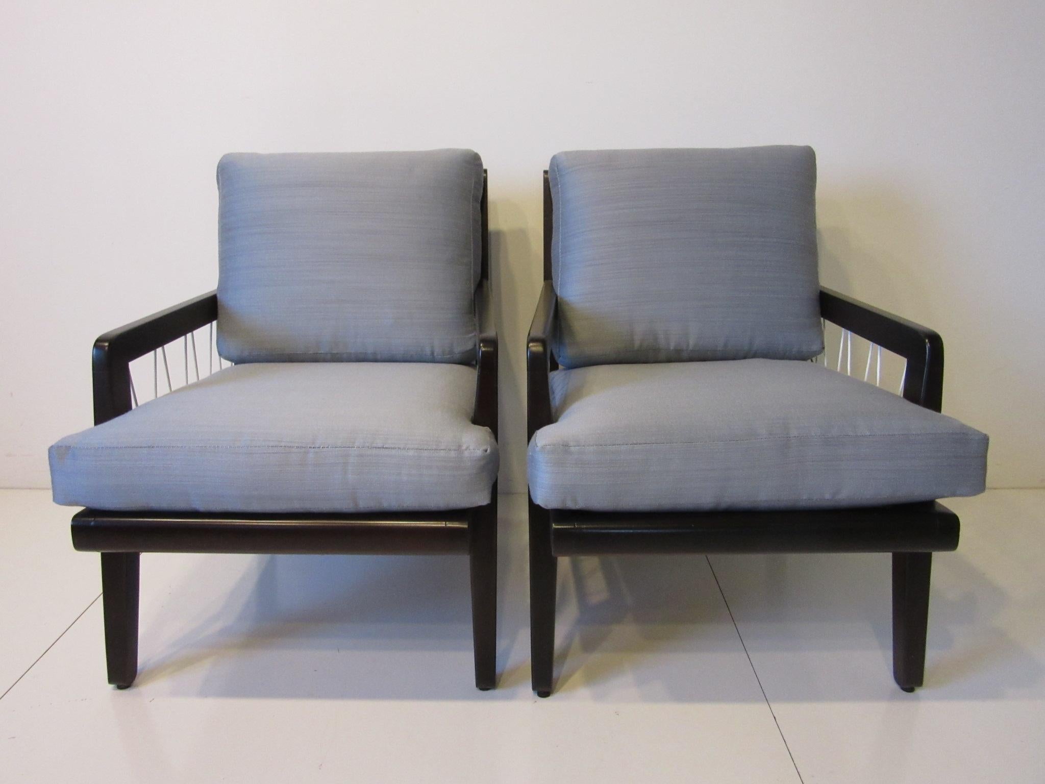 A pair of ebony toned solid wood framed lounge chairs with nylon cord design to the open arm and back areas, the two cushion chairs are upholstered in a fine soft sophisticated contract fabric with lines of lighter and darker grays. Designed for