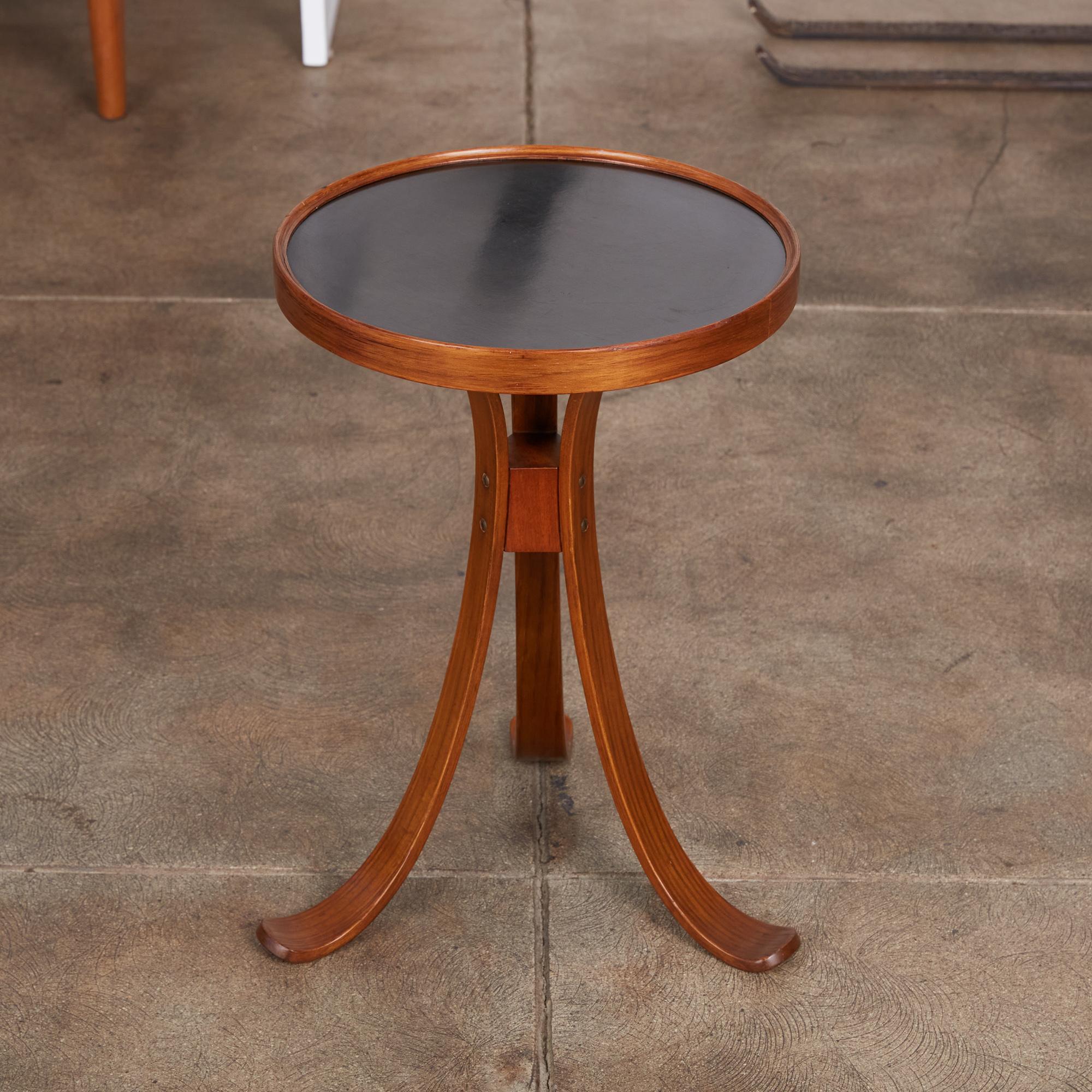 A tripod side table by Edward Wormley for Dunbar, c.1960s. The table features an oiled mahogany frame, curved bentwood tripod legs and a round black laminate top with raised edge. This small table is perfect for drinks or anywhere a side table with