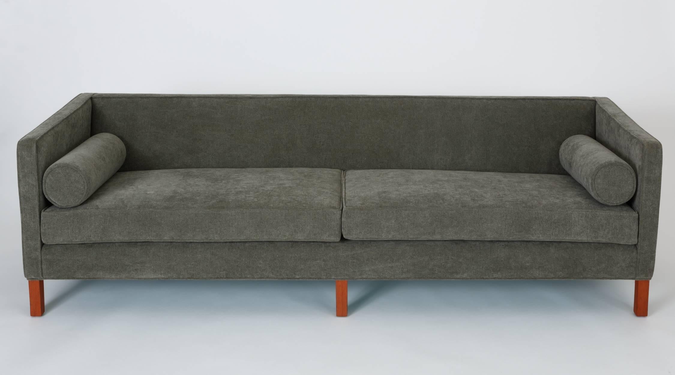 A straightforward modern design from Edward Wormley, this 1950s sofa has a three-sided, upholstered case with a back panel gently angled for comfort. The deep seat has two long cushions and a tight back, flanked on either side by round bolster