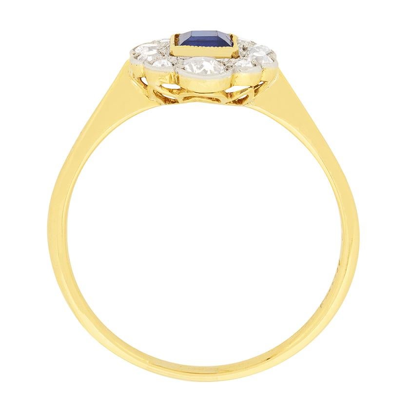 A beautiful carre cut sapphire is showcased in this Edwardian cluster ring. It is a deep blue colour, which is accented by the 18 carat yellow gold rub over setting. Old cut diamonds surround the sapphire, totalling to 0.58 carat. They are H to I in