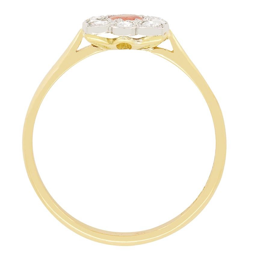 Un raro zaffiro arancione occupa il posto d'onore in questo splendido anello a grappolo edoardiano. Con un peso di 0,40 carati, lo zaffiro dal taglio ovale ha una vibrante tonalità arancione che contrasta meravigliosamente con la montatura in