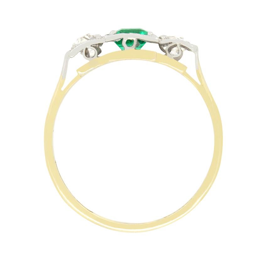 Dating back to the Edwardian era, this beautiful trilogy ring features a central emerald, flanked by old cut diamonds in a unique stepped box setting. The central emerald is a classic emerald cut stone weighing 0.50 carat. Each of the accompanying