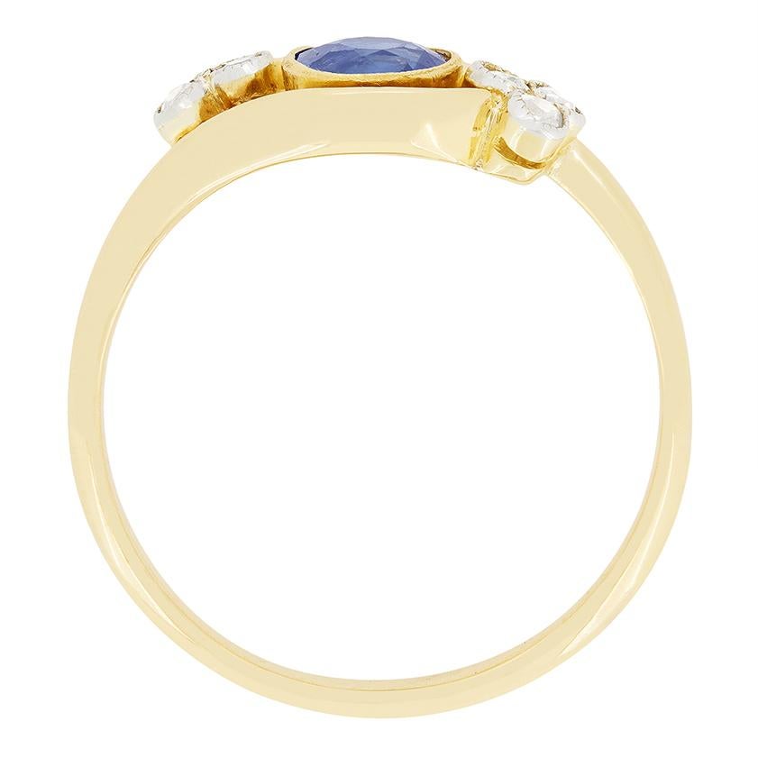 This beautiful twisted cluster ring dates to the Edwardian period. An oval cut sapphire sits central to the piece with clusters of old cut diamonds set to either side. Rub over set into 18 carat yellow gold the sapphire weighs 0.50 carat and is a