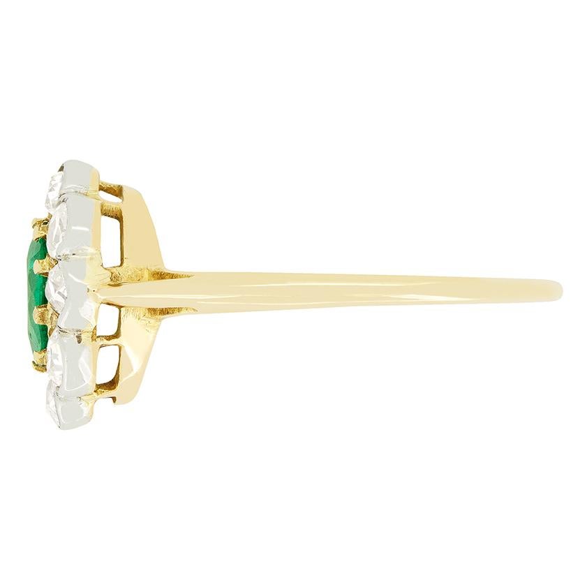 This beautiful cluster ring dates to the Edwardian era and centres around a vibrant natural emerald. The 0.60 carat emerald is an old oval cut stone set within 18 carat yellow gold claws. Enveloping the central stone a collection of old cut diamonds