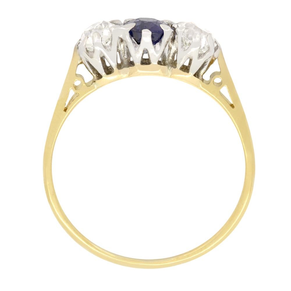 This beautiful trilogy ring features a central sapphire with a pair of old cut diamonds flanking. The intense blue sapphire is also an oval cut stone with a weight of 0.60 carat. The two diamonds weigh 0.40 carat each and match in quality at G in