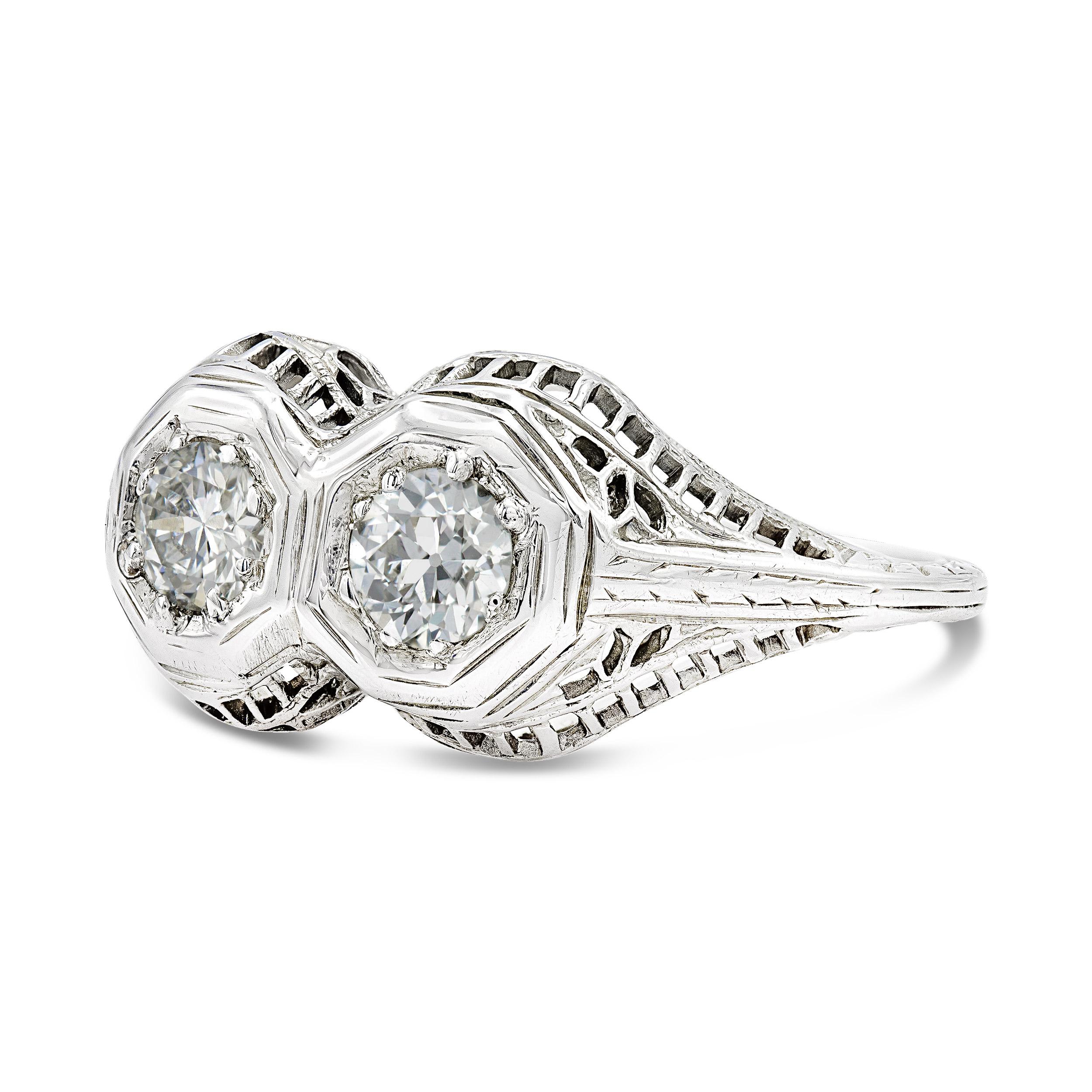 Edwardian era rings are distinguished by intricate filigree and unique accents. This toi-et-moi style ring features twin old European cut diamonds bezel-set and shining brightly. There is so much added intrigue in the metalwork along the gallery and