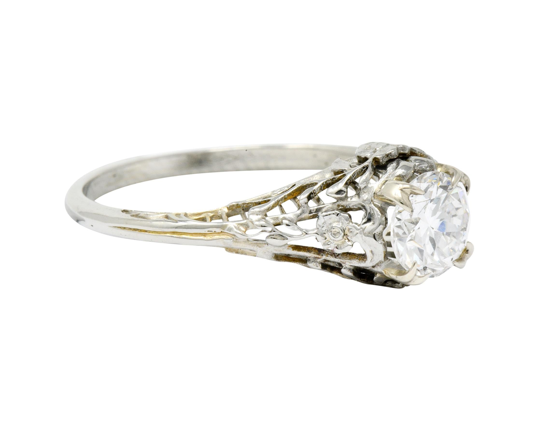 Centering a transitional cut diamond weighing 0.73 carat, F color with VS2 clarity

Prong set in a pierced decorative mount featuring a floral motif at each cardinal point

Completed by vine-like foliate filigree throughout shoulders and