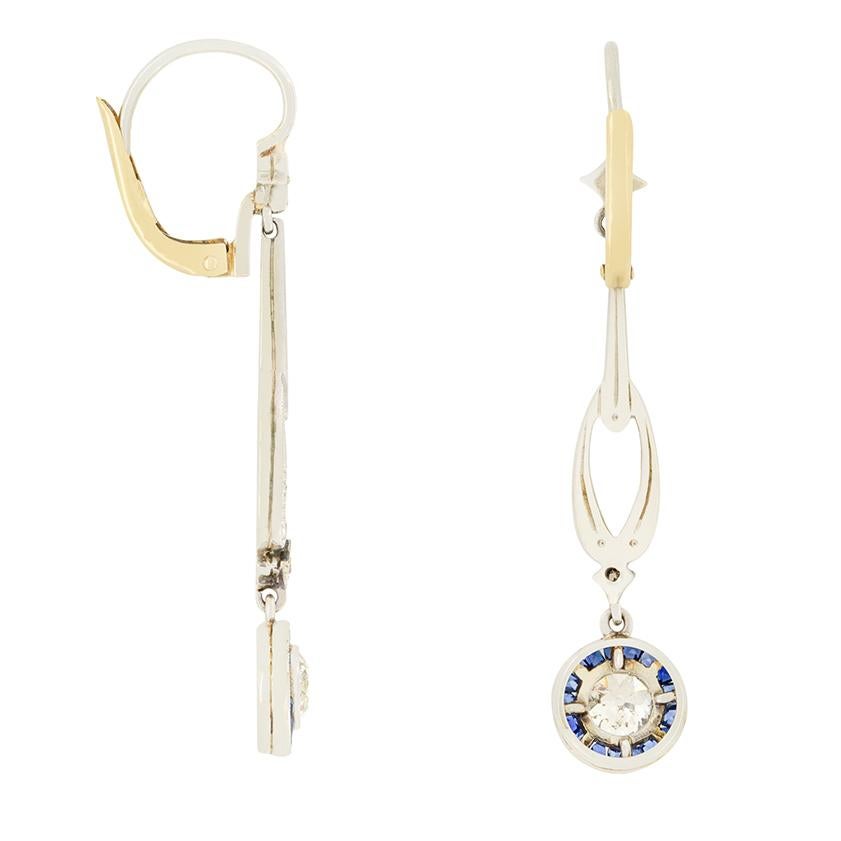 These exquisite Edwardian drop earrings feature a classic target design at the bottom of each drop. A 0.40 carat old cut diamond is beautifully rub over set, encircled by 0.40 carat  of deep blue baguette cut sapphires, creating the stunning target