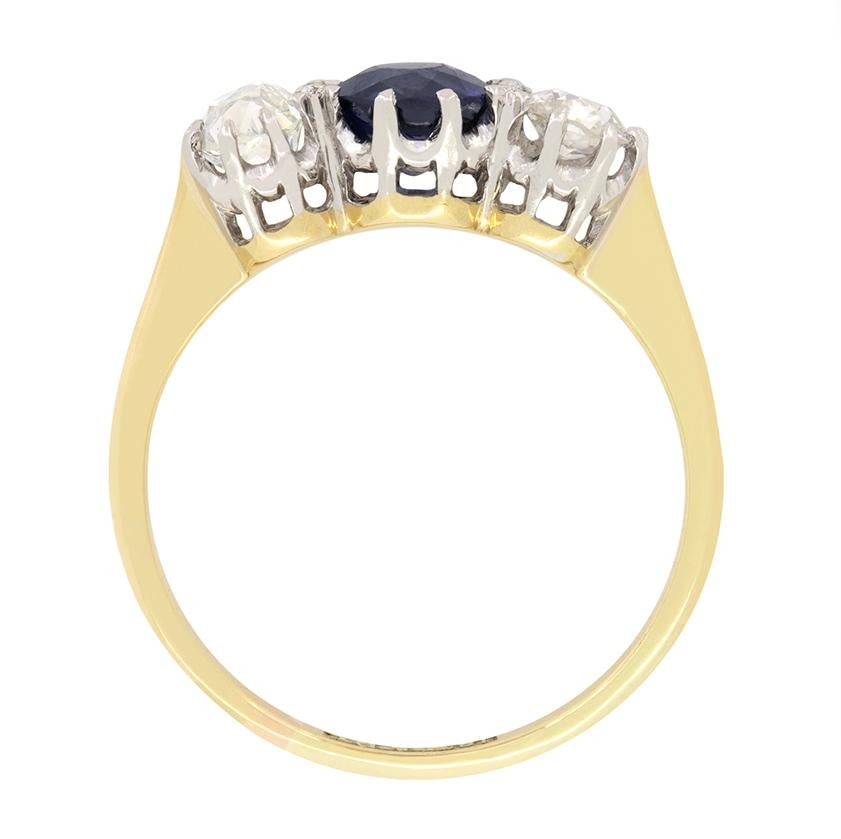 Cette superbe bague édouardienne à trois pierres met en valeur un saphir bleu profond en son centre, flanqué de deux diamants de taille ancienne. Le saphir est une pierre de taille ancienne pesant 0,85 carat. Chacun des diamants qui l'accompagnent